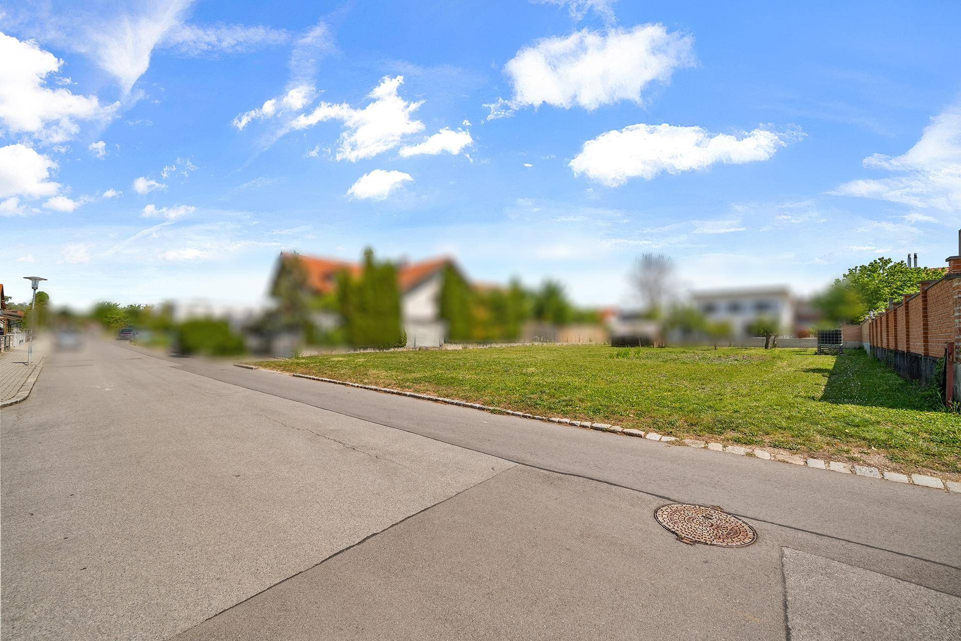 Blick von der Straße auf ein großes, unbebautes Grundstück mit Rasenfläche und umliegenden Häusern.