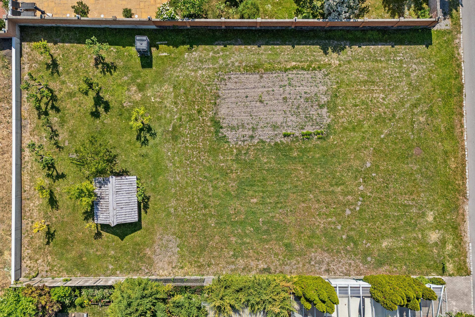 Vogelperspektive eines Gartengrundstücks mit Rasen, einem Beet, jungen Bäumen und einem kleinen Schuppen.