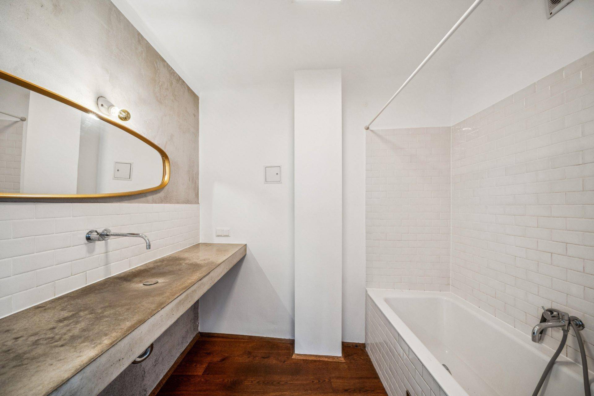Modernes Badezimmer mit langer Waschtischplatte aus Betonoptik und Badewanne.