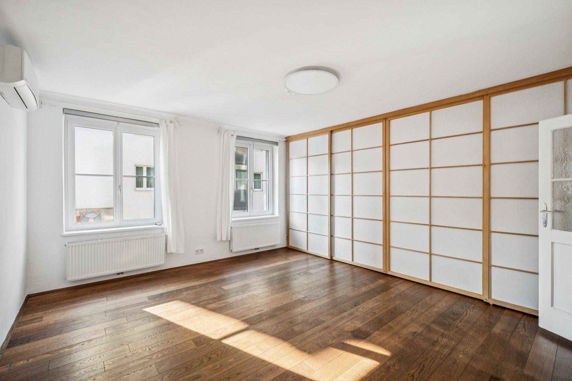 Leeres Schlafzimmer mit Holzboden, großen Fenstern und integrierten Schiebetüren.