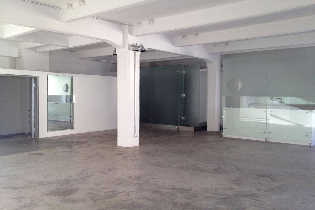 Weitläufiger, heller Loftraum mit Betonboden, hohen Decken und modernen Glasabtrennungen.