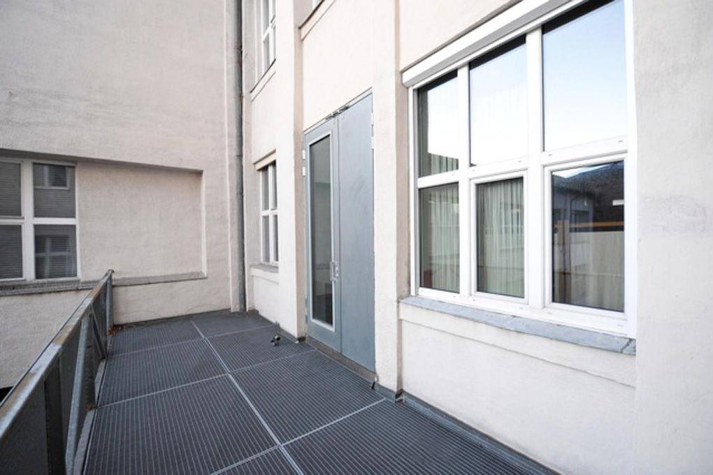Schmaler Außenbalkon mit Metallgitterboden und Zugang zu einem Gebäude.