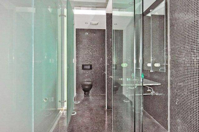 Modernes Badezimmer mit dunklen Mosaikfliesen, wandhängendem WC und Glasdusche.