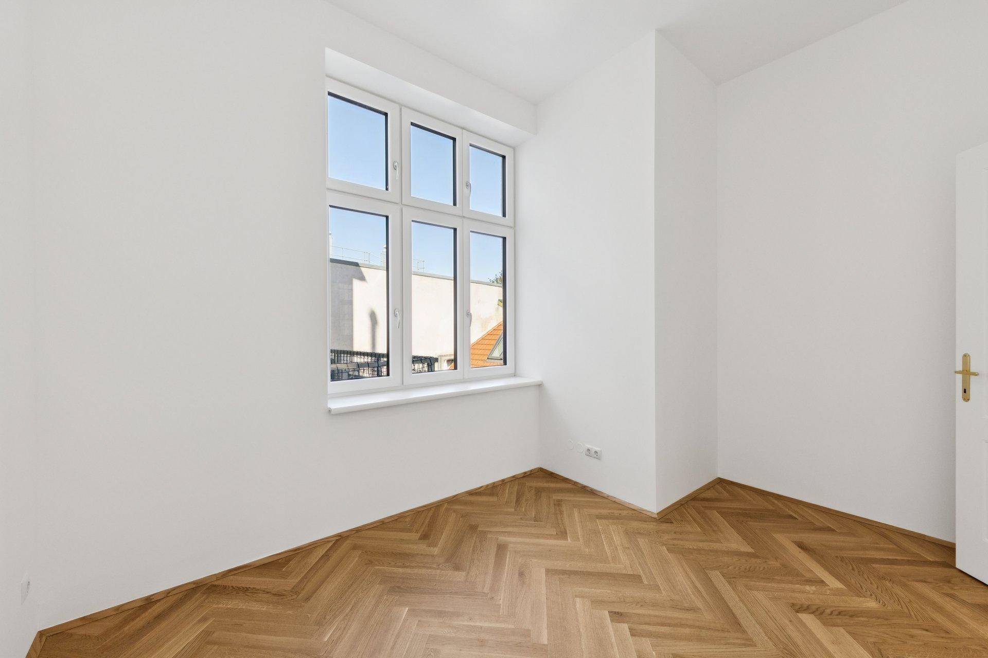 Ruhiges Zimmer mit Fischgrätparkett und einem großen Fenster, ideal als Schlaf- oder Arbeitszimmer.