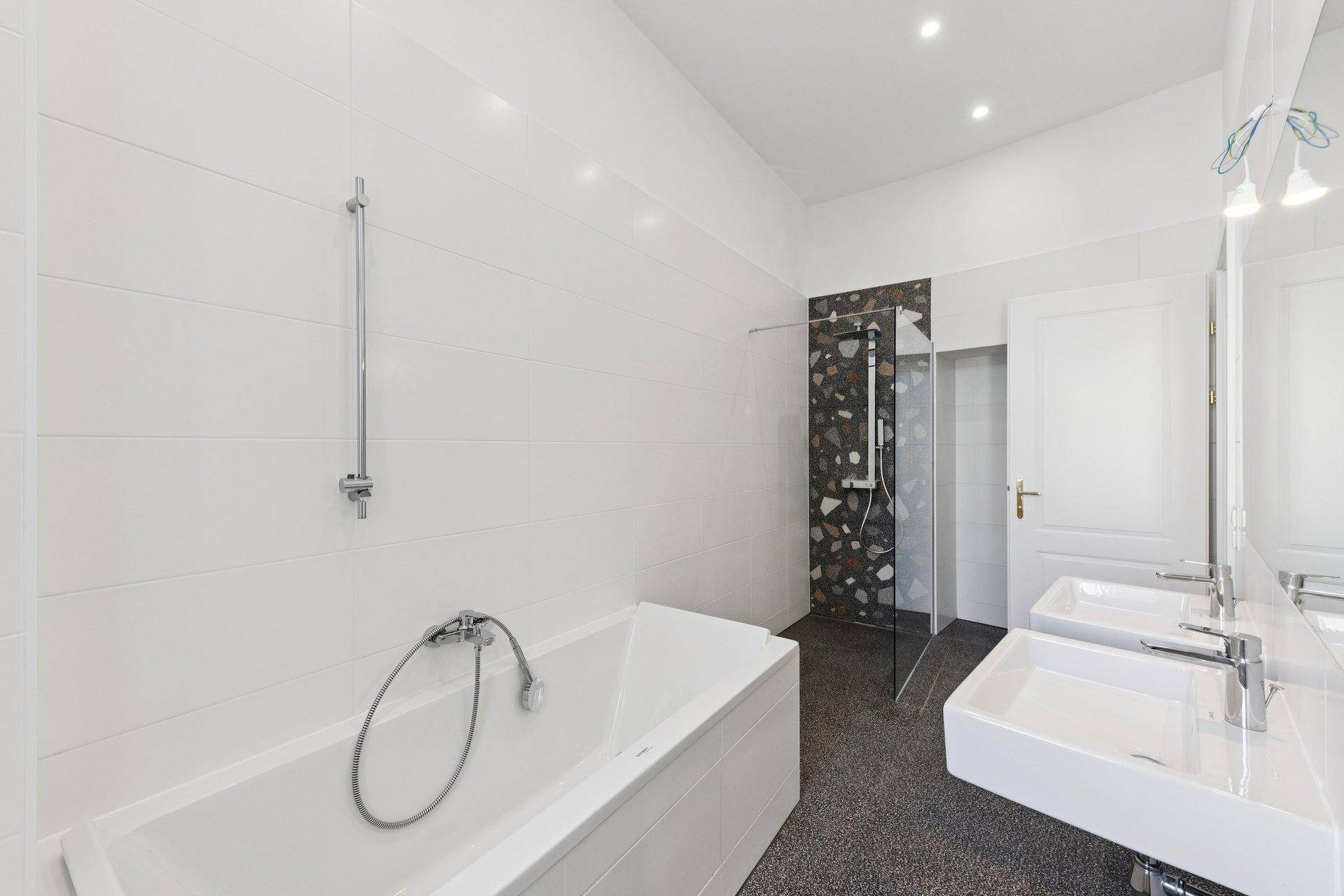 Modernes Badezimmer mit weißen Fliesen, begehbarer Dusche, Badewanne und Doppelwaschbecken.