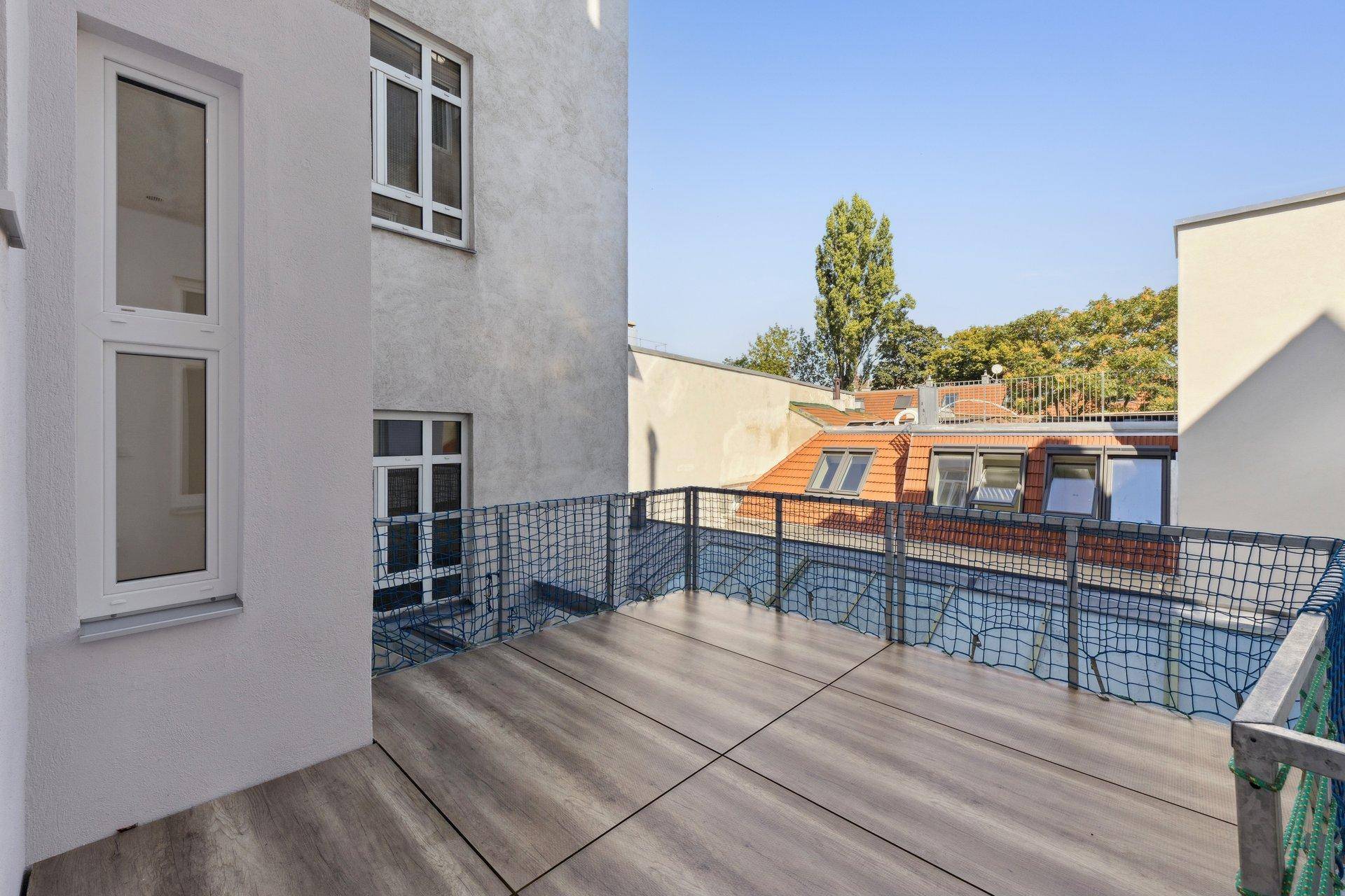 Geräumiger Balkon mit Fliesenboden und Blick auf umliegende Gebäude und Bäume.