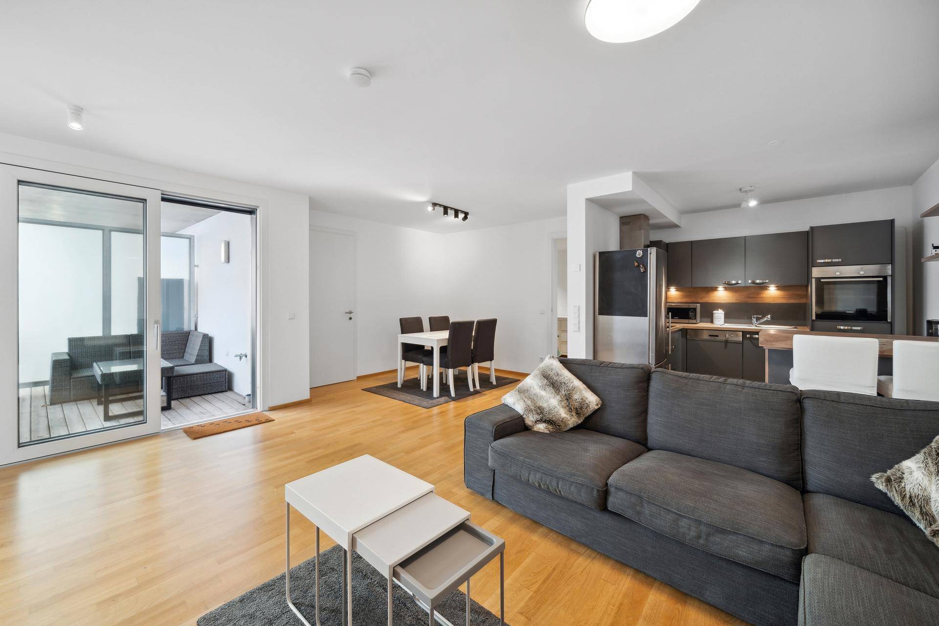 Heller offener Wohn-Essbereich mit integrierter Küche, Holzboden und Zugang zum Balkon.