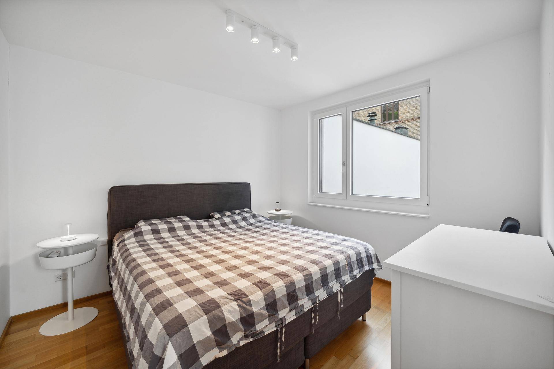 Helles Schlafzimmer mit Doppelbett, Holzboden und Fenster mit Blick auf den Innenhof.
