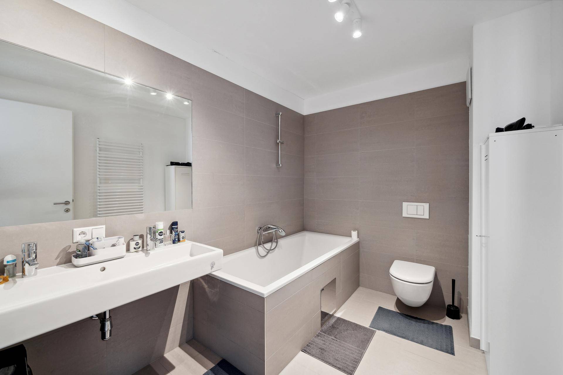 Modernes Badezimmer mit Badewanne, Wand-WC, Einzelwaschbecken und grauen Fliesen.