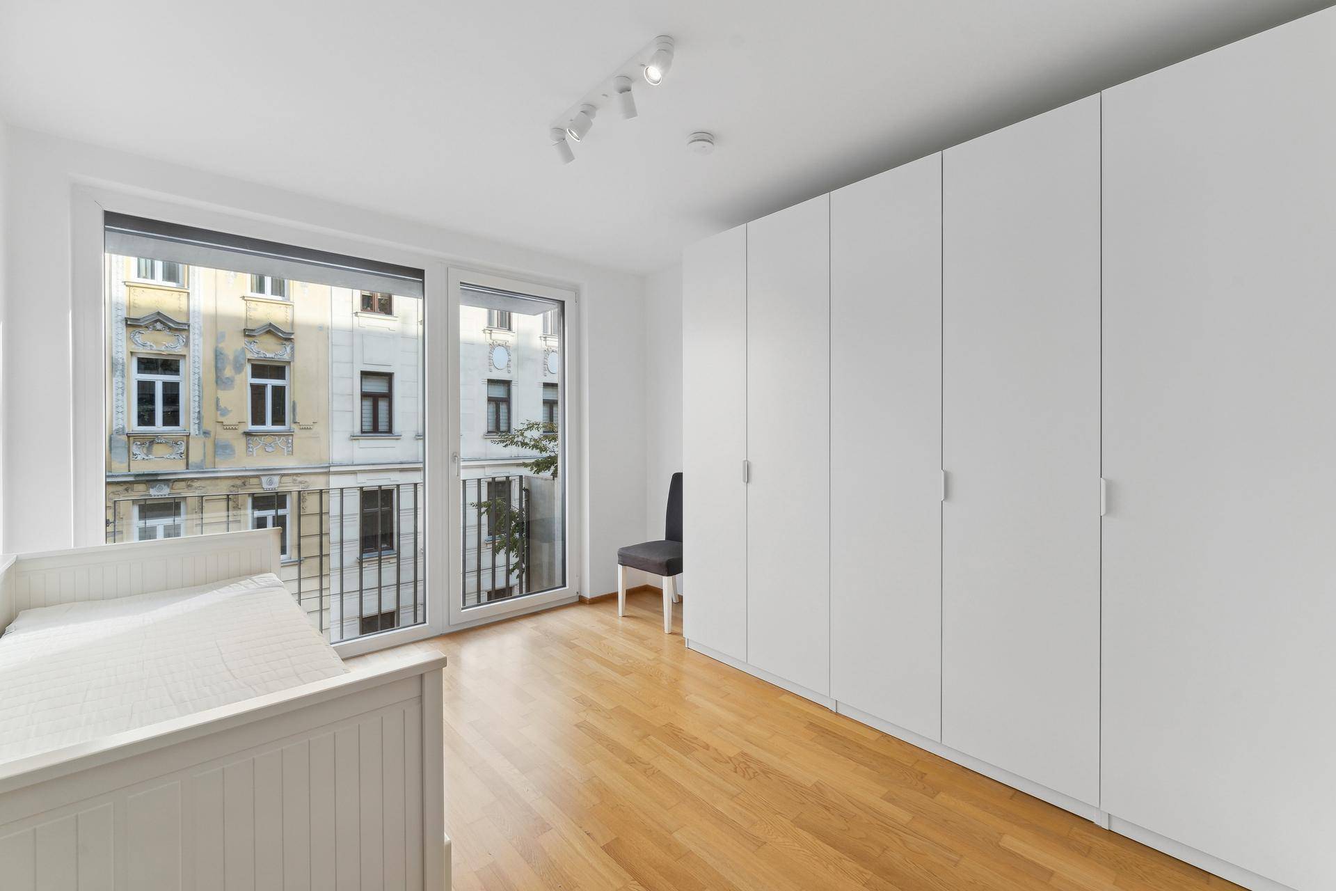 Helles Schlafzimmer mit Einbauschränken, Holzboden und großem Fenster mit Stadtblick.