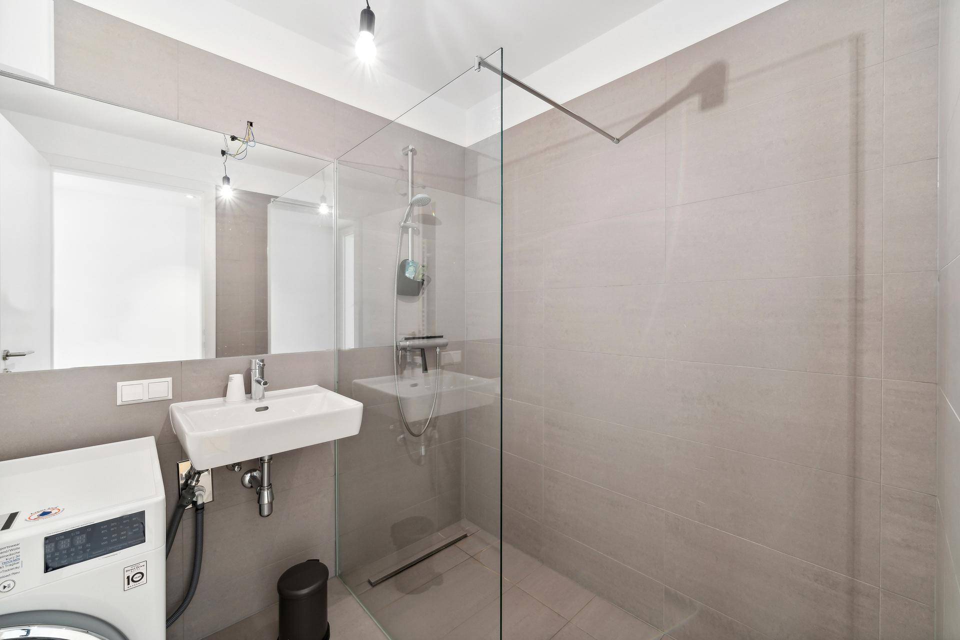 Zeitgemäßes Badezimmer mit ebenerdiger Dusche, Waschbecken und integrierter Waschmaschine.