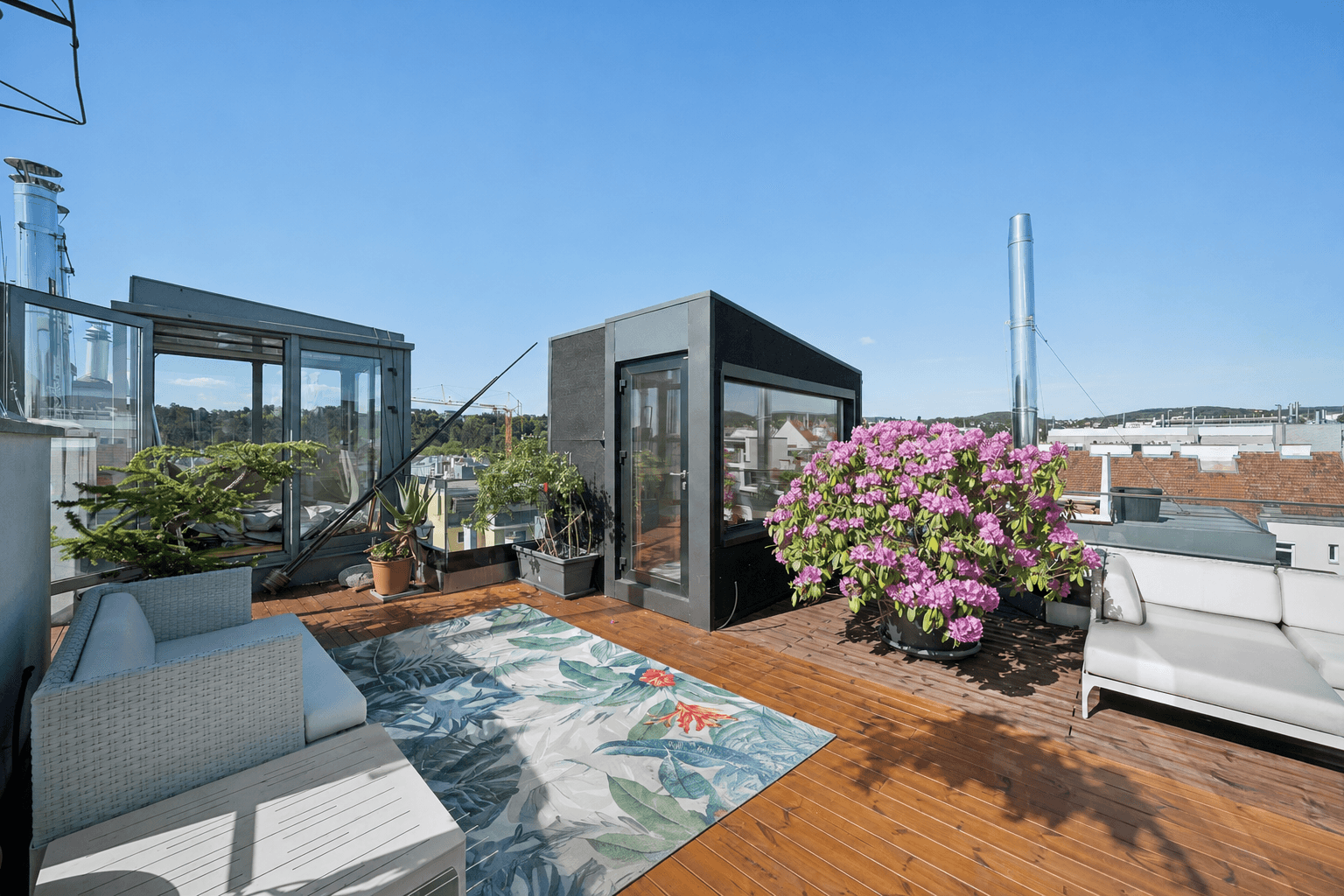 Weitläufige Dachterrasse mit modernen Sitzmöbeln, blühenden Pflanzen und Zugang zu den Innenräumen.