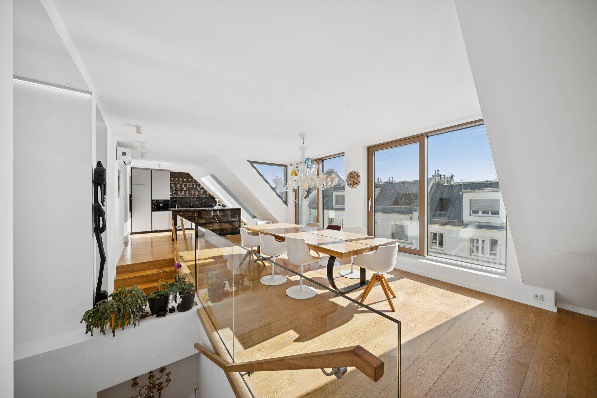 Offener Wohn- und Essbereich mit Holzboden, großen Fenstern und moderner Treppe.