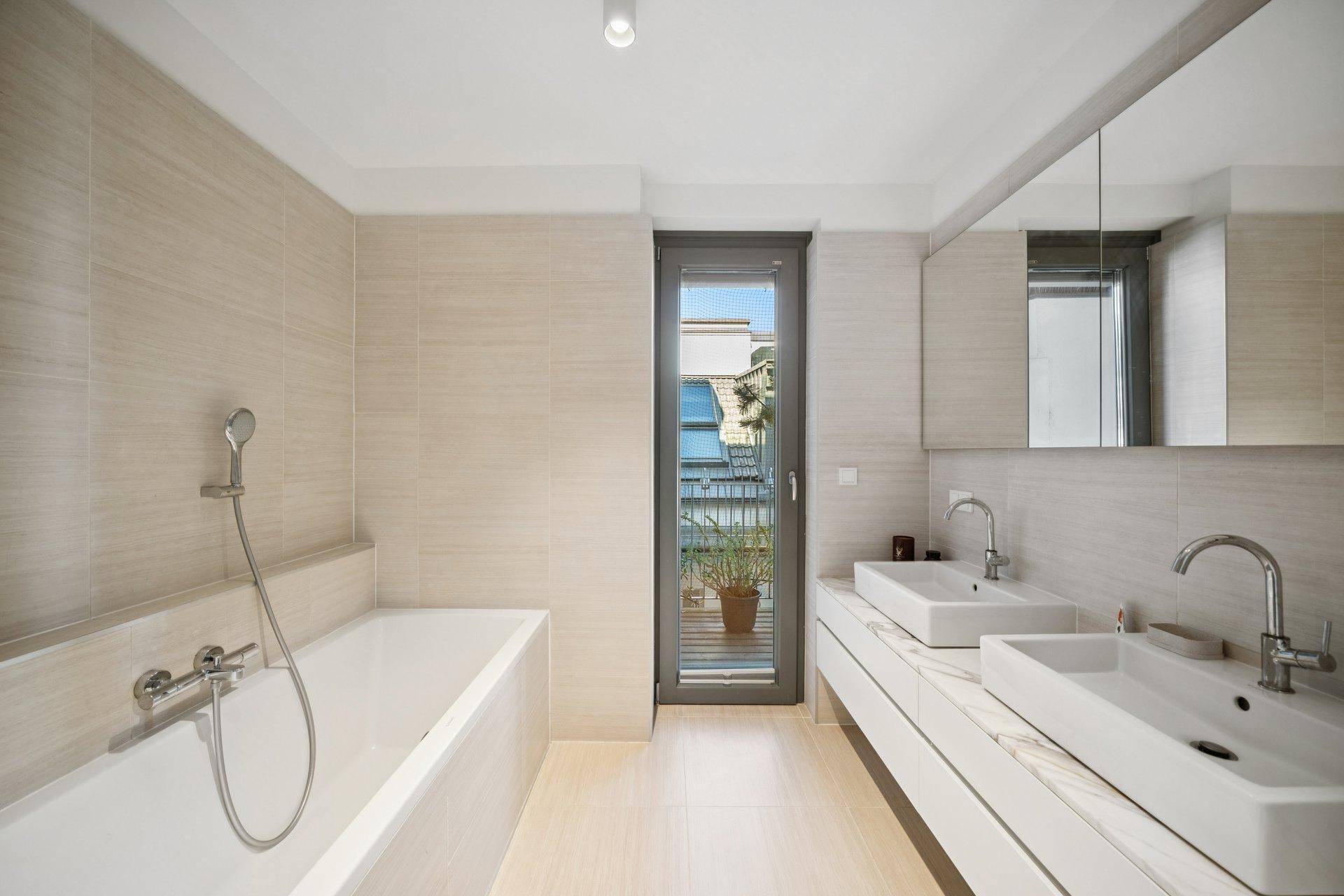 Modernes Badezimmer mit Doppelwaschbecken, Badewanne und Zugang zu einem kleinen Außenbereich.