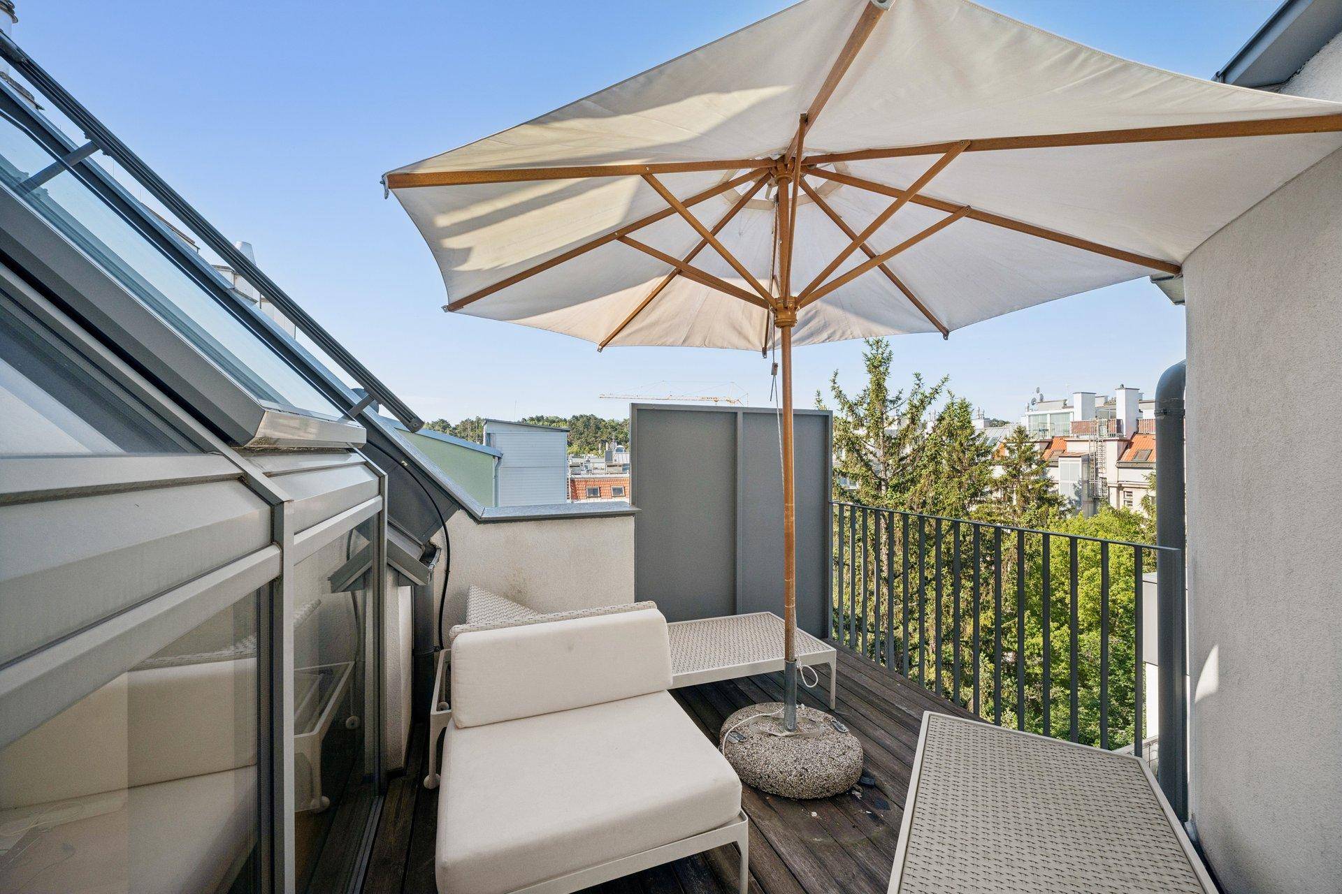 Kleiner Balkon mit Sitzgelegenheiten, Sonnenschirm und grünem Ausblick auf die Umgebung.