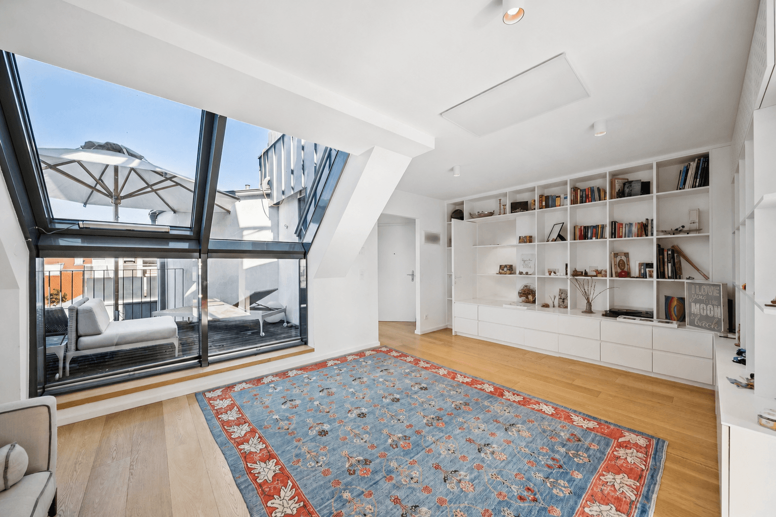Geräumiger Wohnbereich mit maßgefertigtem Bücherregal, Holzboden und Zugang zur Terrasse.