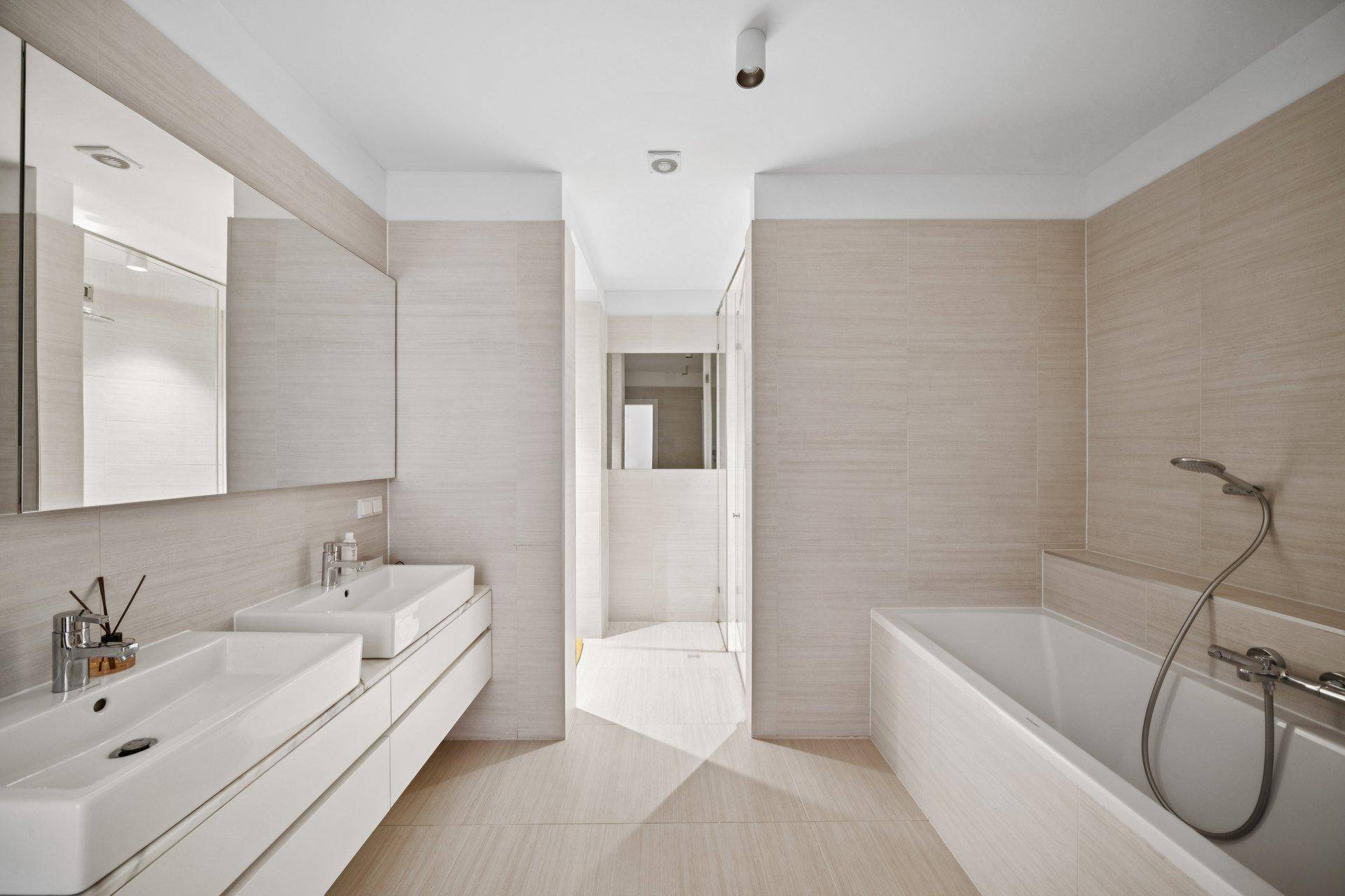 Modernes Badezimmer mit Doppelwaschbecken, Badewanne und hellen Fliesen.