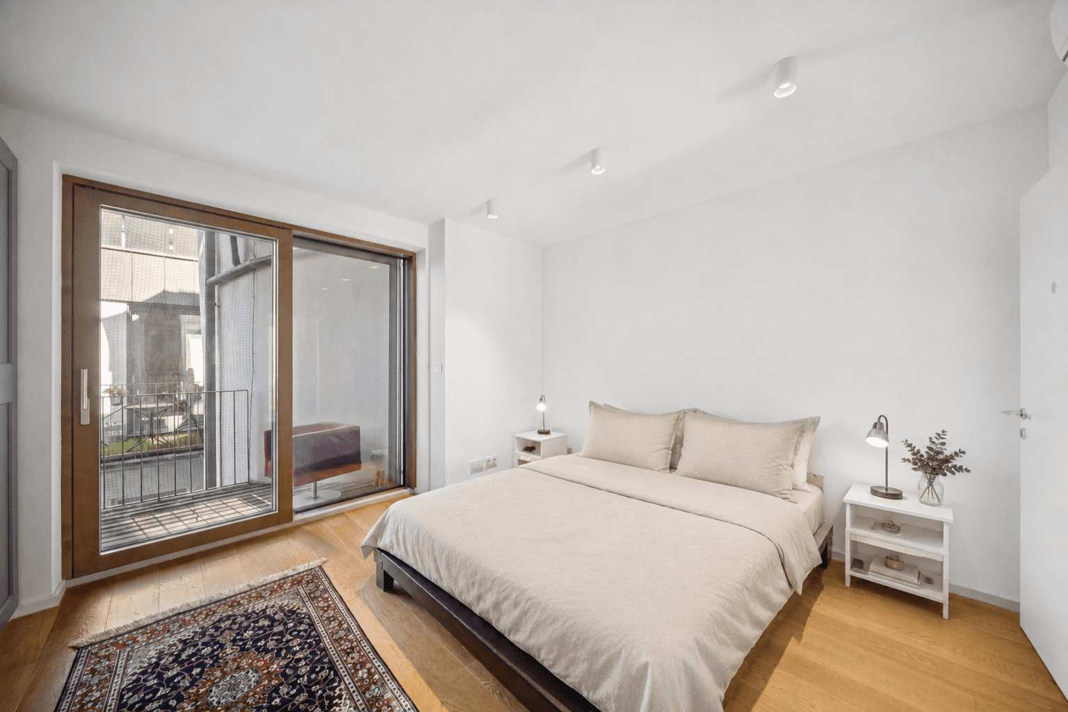 Helles Schlafzimmer mit Doppelbett, Holzboden und direktem Zugang zum Balkon.