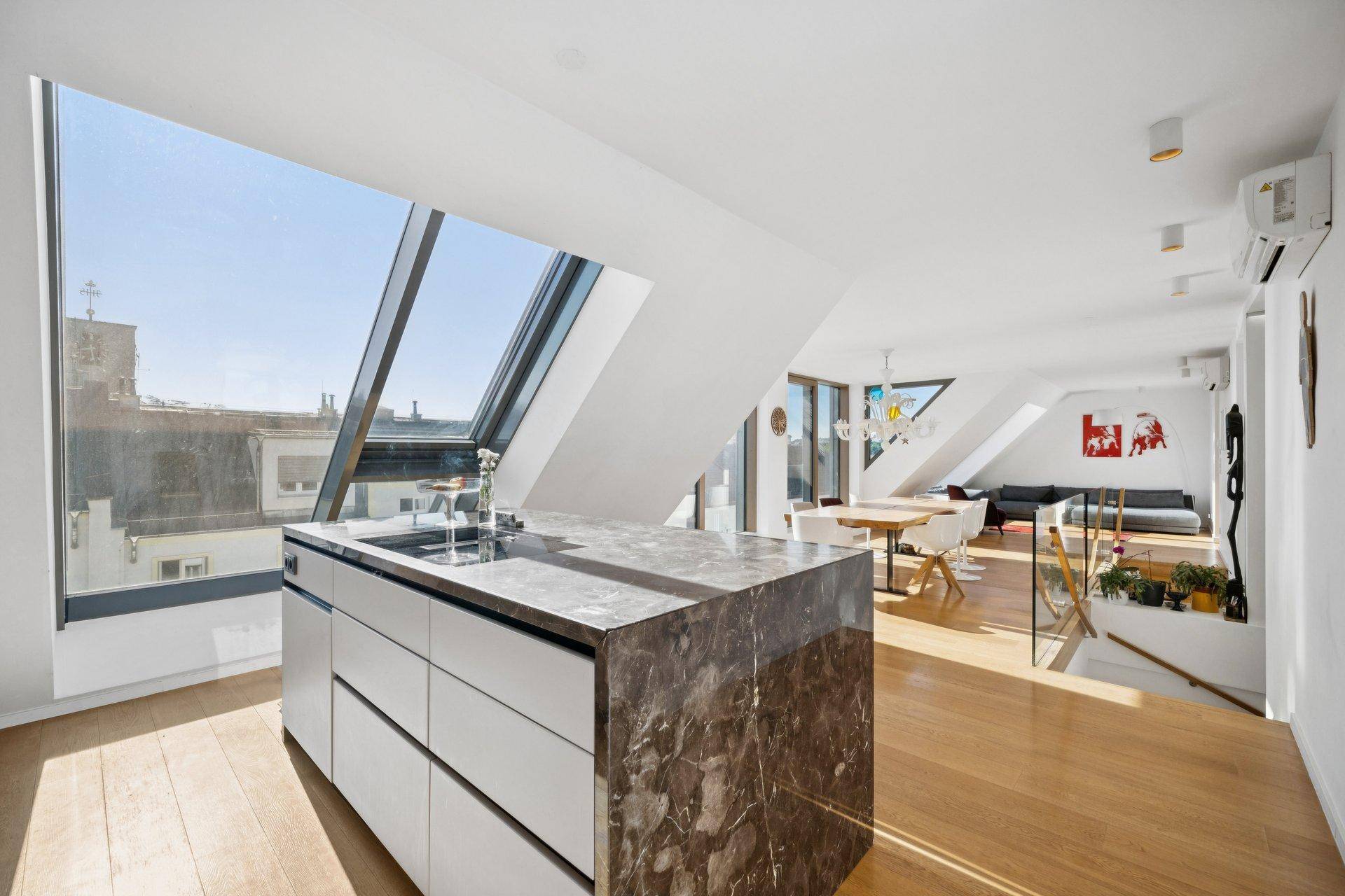Moderne Küche mit Kochinsel, Marmorarbeitsplatte und weitem Blick durch große Dachfenster.