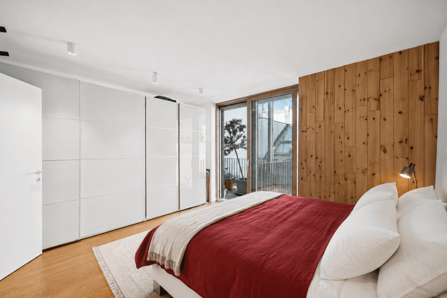 Schlafzimmer mit Holzakzentwand, weißen Einbauschränken und Zugang zu einem Außenbereich.