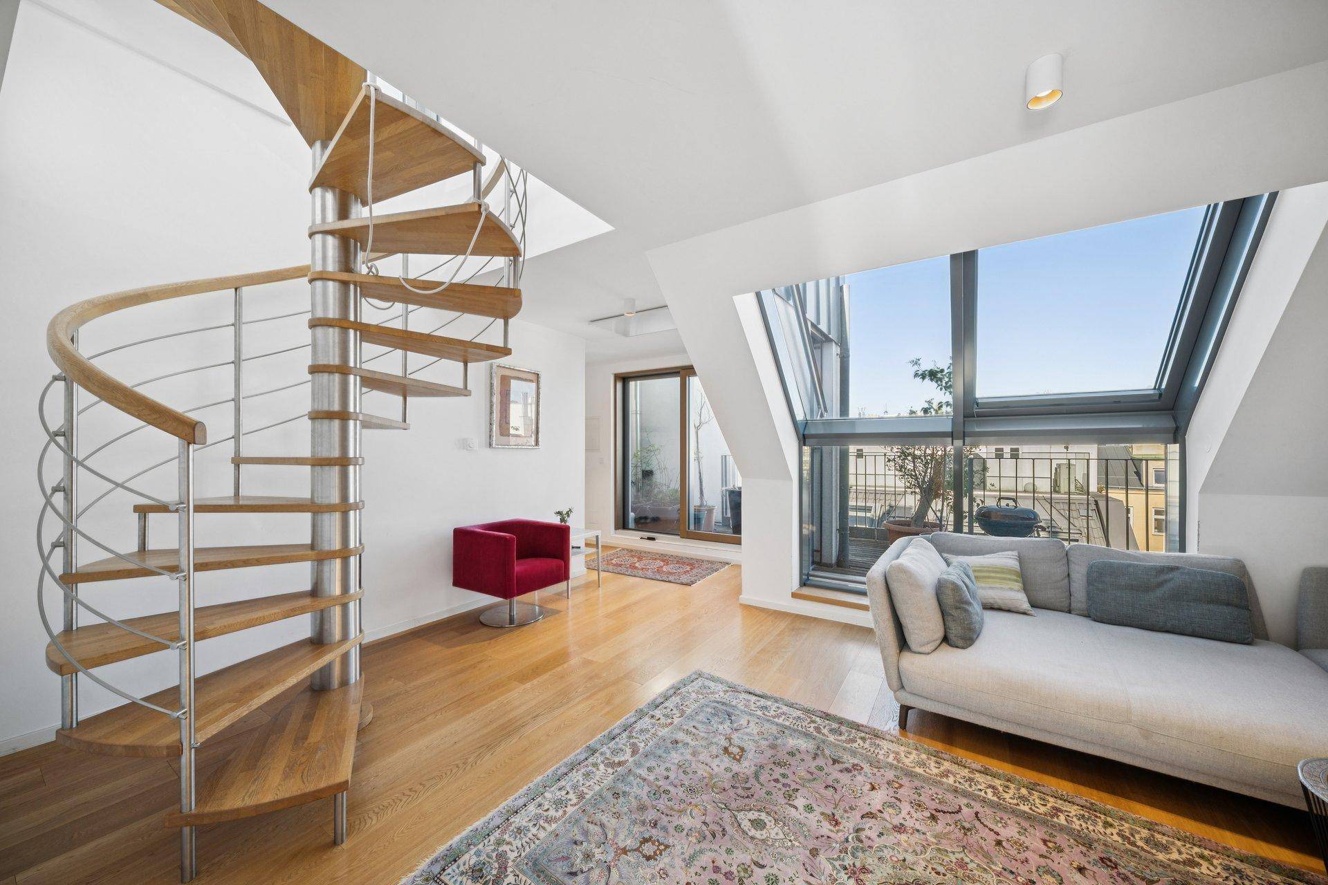 Heller Wohnbereich mit eleganter Wendeltreppe, bequemer Couch und großen Fenstern.