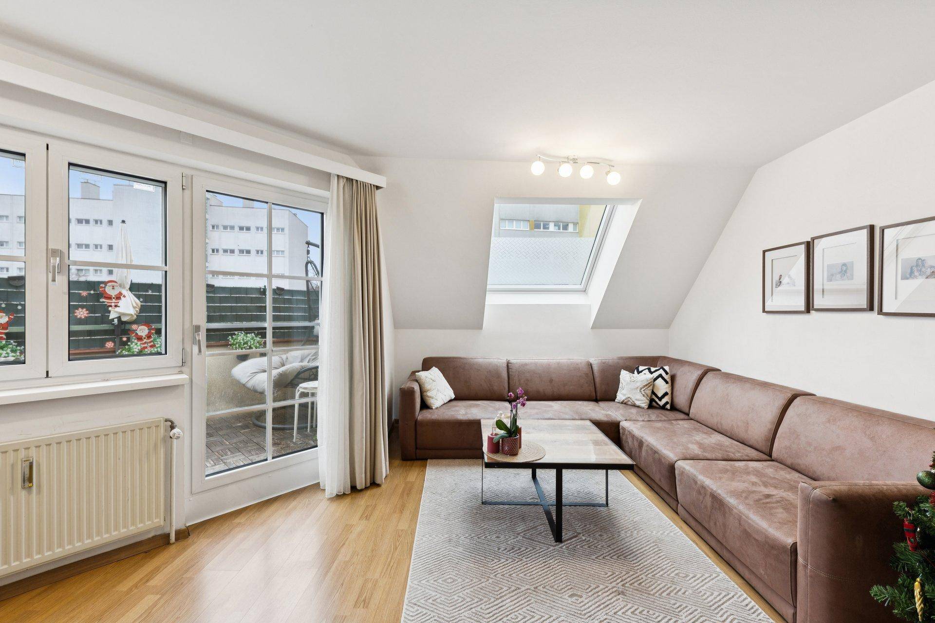 Gemütliches Wohnzimmer mit großer Eckcouch, Holzboden und viel Tageslicht durch Fenster und Dachfenster.