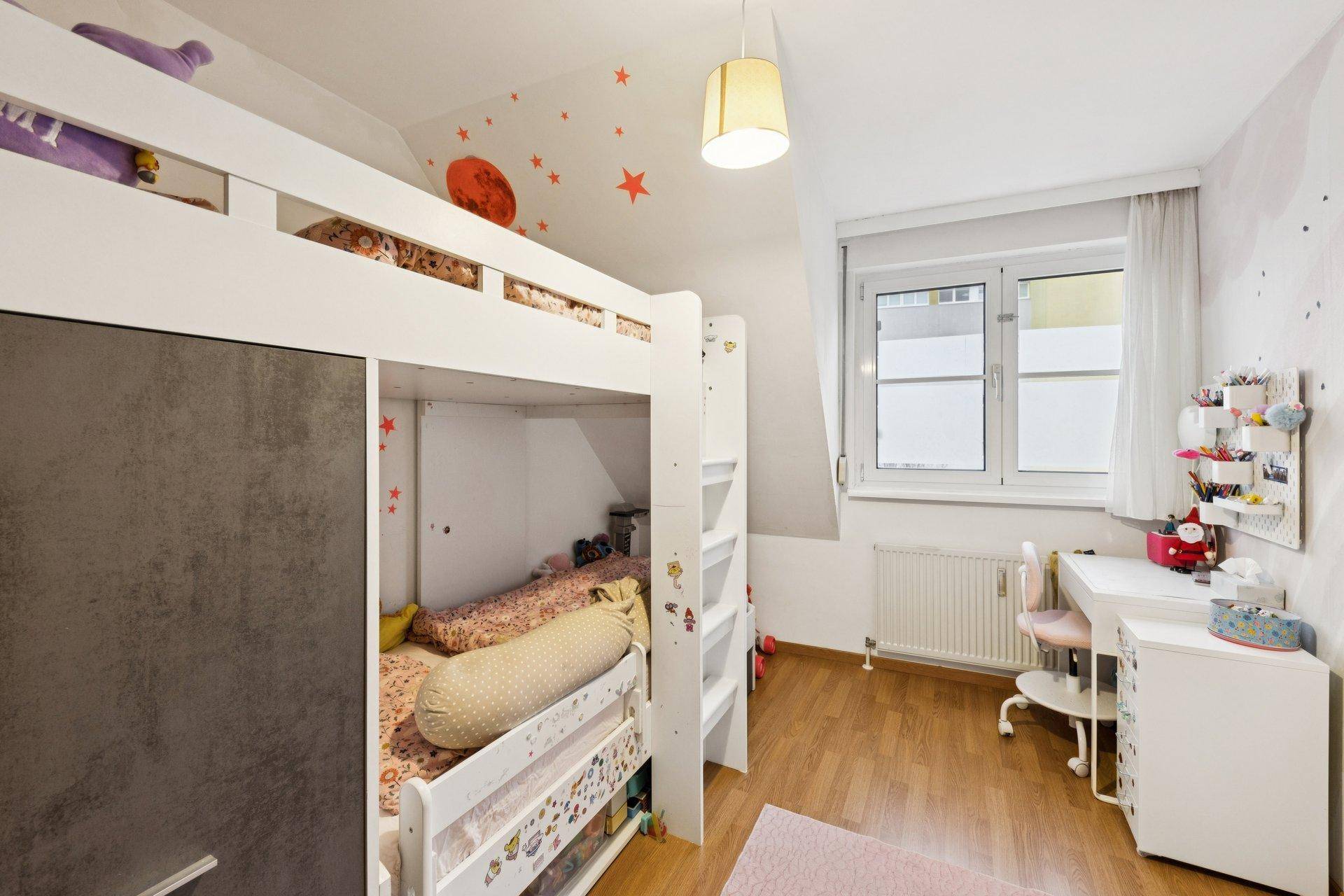 Helles Kinderzimmer mit Etagenbett, Schreibtisch und Holzboden, ideal für junge Bewohner.
