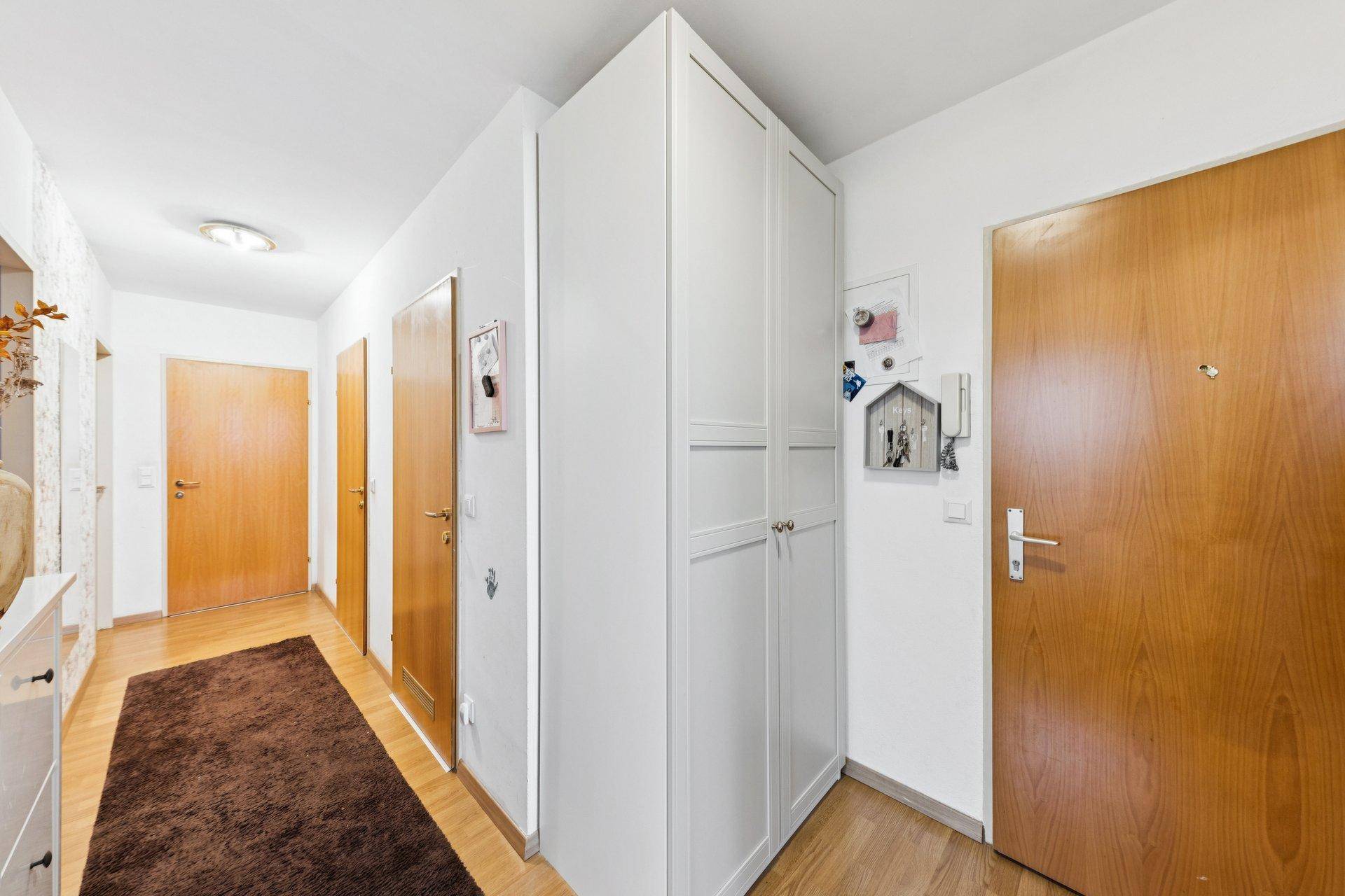Heller Flur mit Holztüren, praktischen Einbauschränken und einem Teppich auf dem Holzboden.