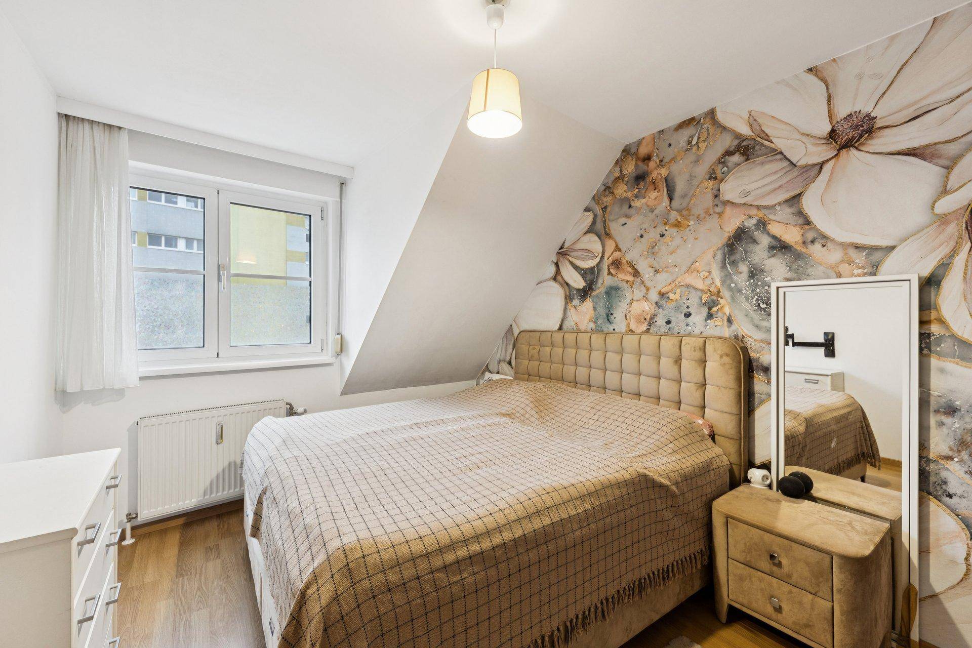 Schlafzimmer mit Doppelbett, Nachttisch und auffälliger floraler Tapetenwand, bietet eine gemütliche Atmosphäre.