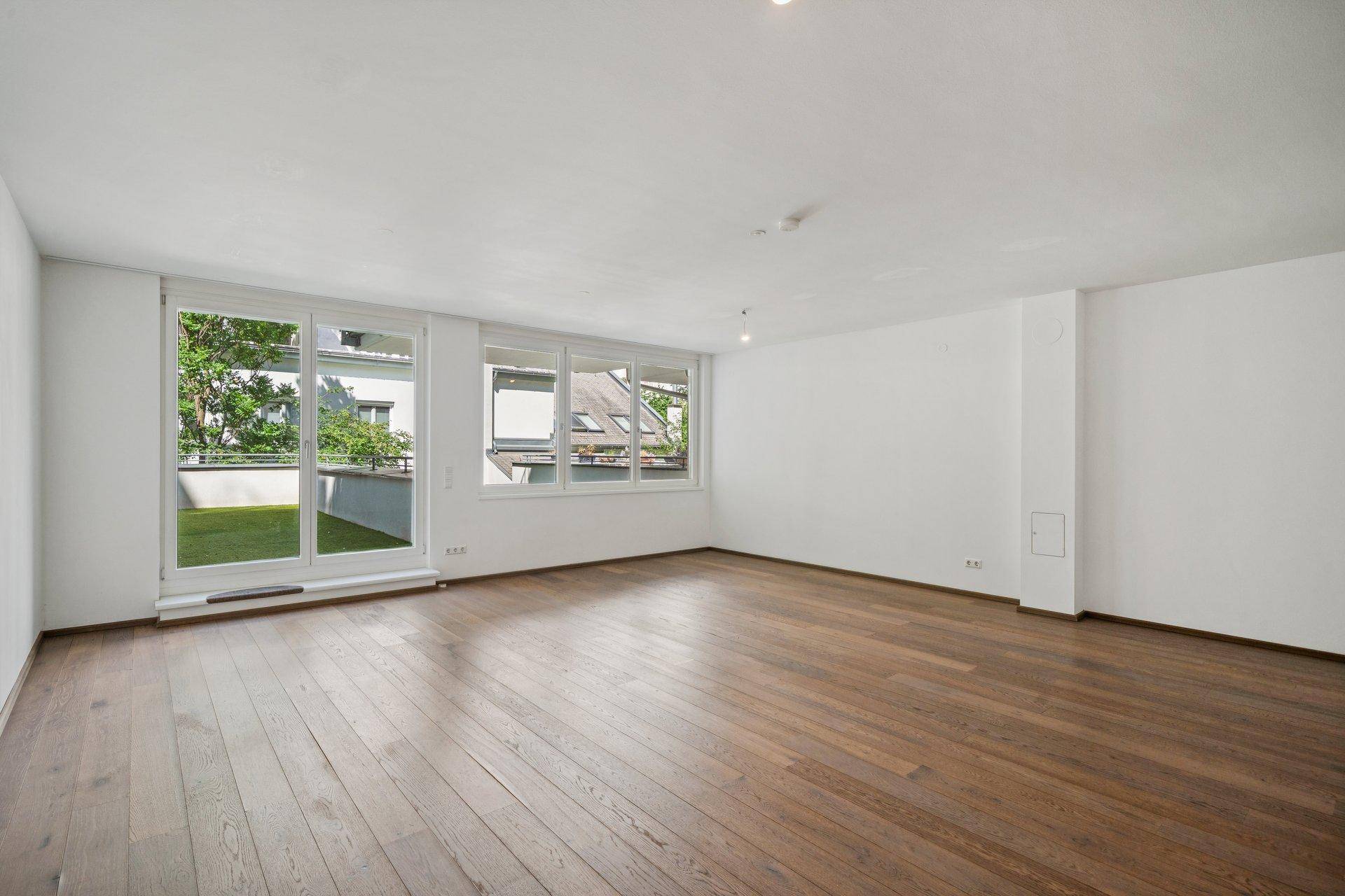 Geräumiger, leerer Raum mit Holzboden und großen Fenstern, die Zugang zur Terrasse bieten.