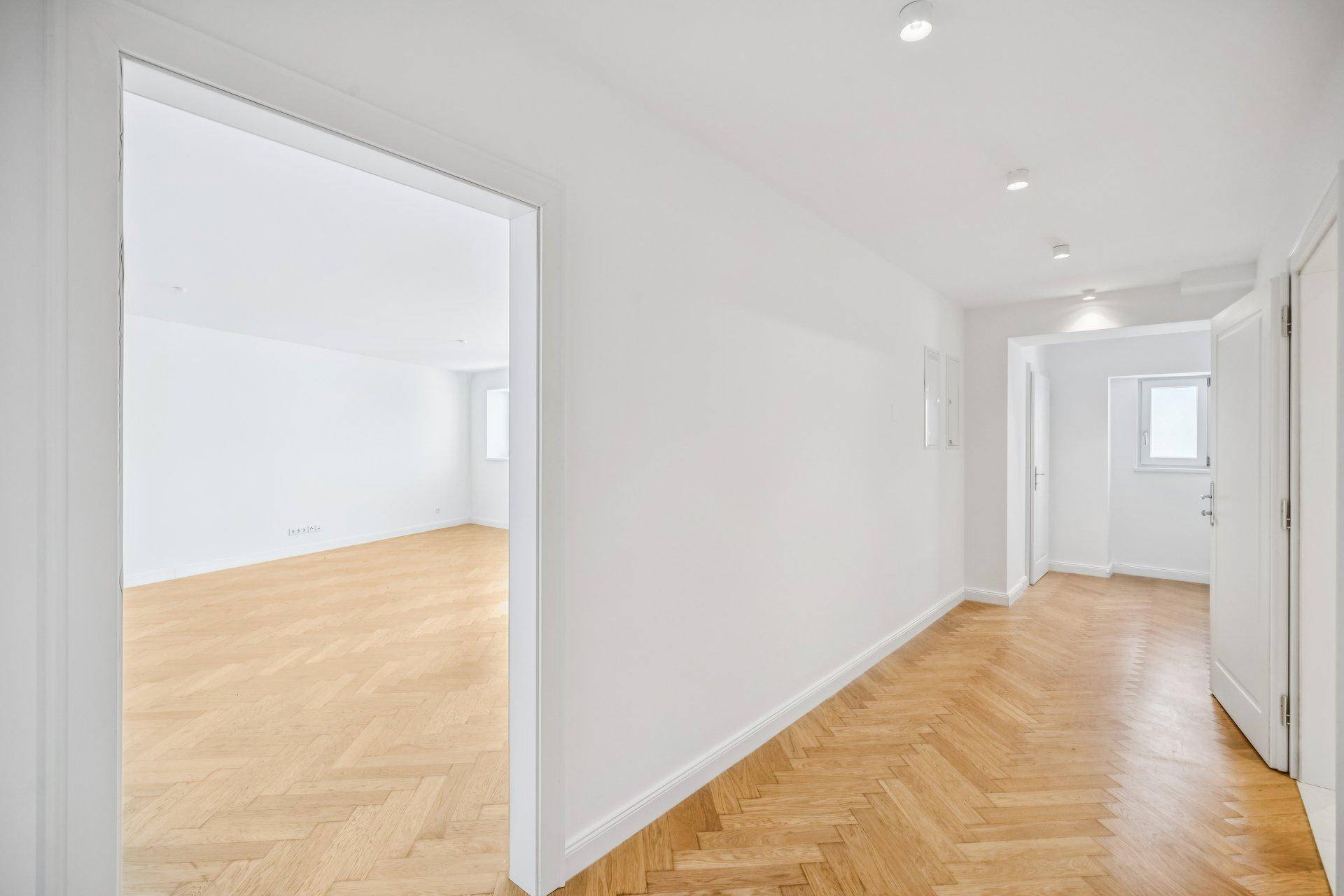 Heller Flur mit Fischgrätparkettboden, der zu weiteren Zimmern der Wohnung führt.