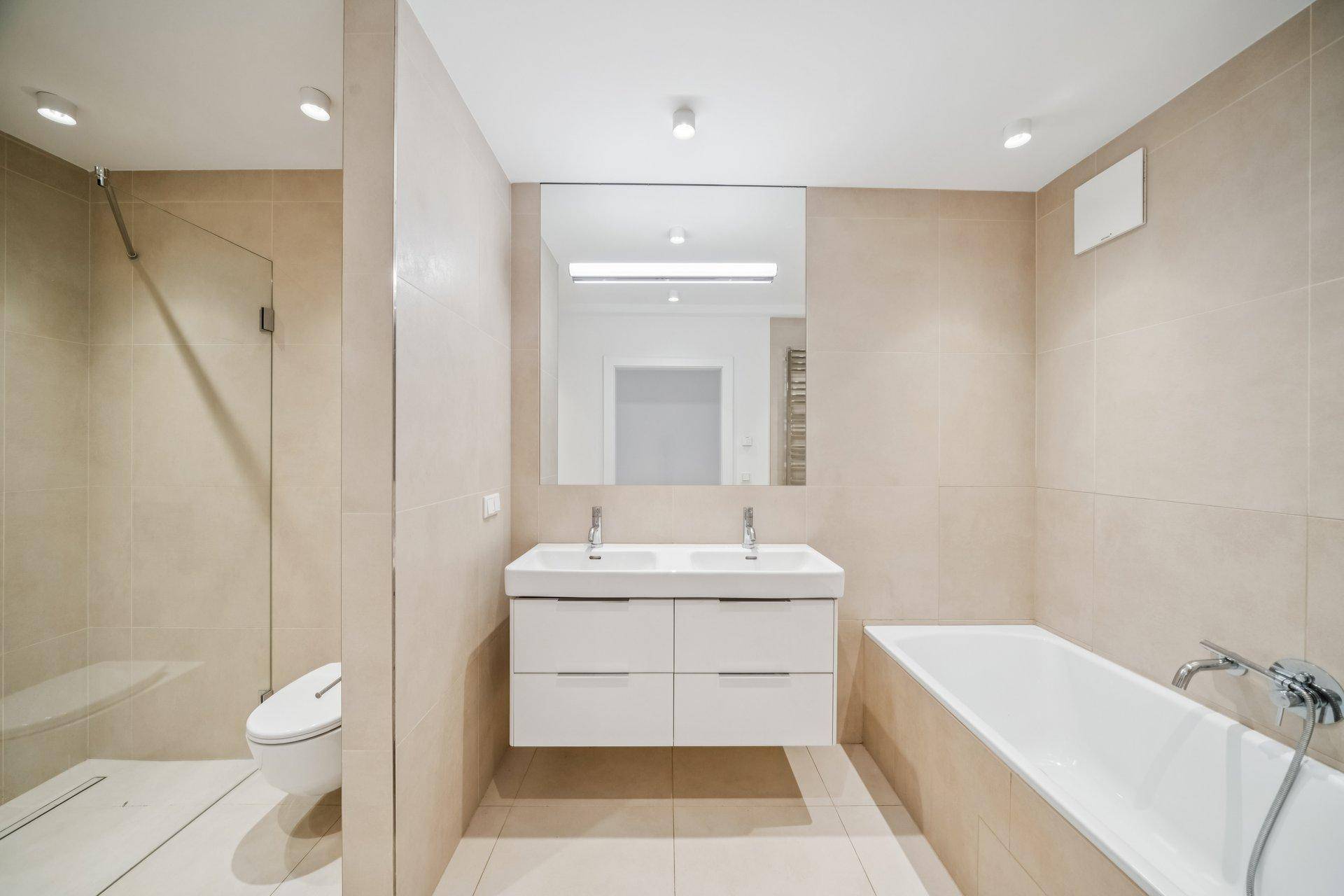 Modernes Badezimmer mit Doppelwaschbecken, Badewanne, begehbarer Dusche und beigefarbenen Fliesen.