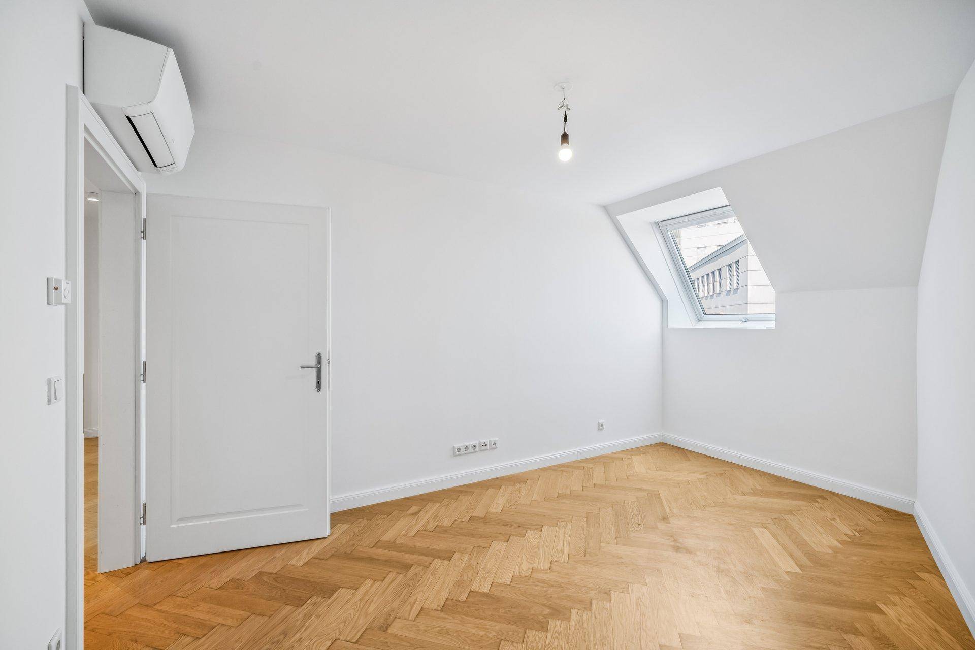 Helles Schlafzimmer im Dachgeschoss mit Dachfenster, Klimaanlage und Fischgrätparkettboden.