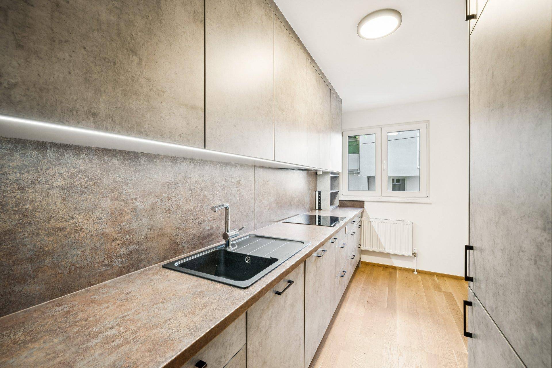 Funktionale Küche mit grauen Schränken, integriertem Kochfeld und einem Fenster für Tageslicht.
