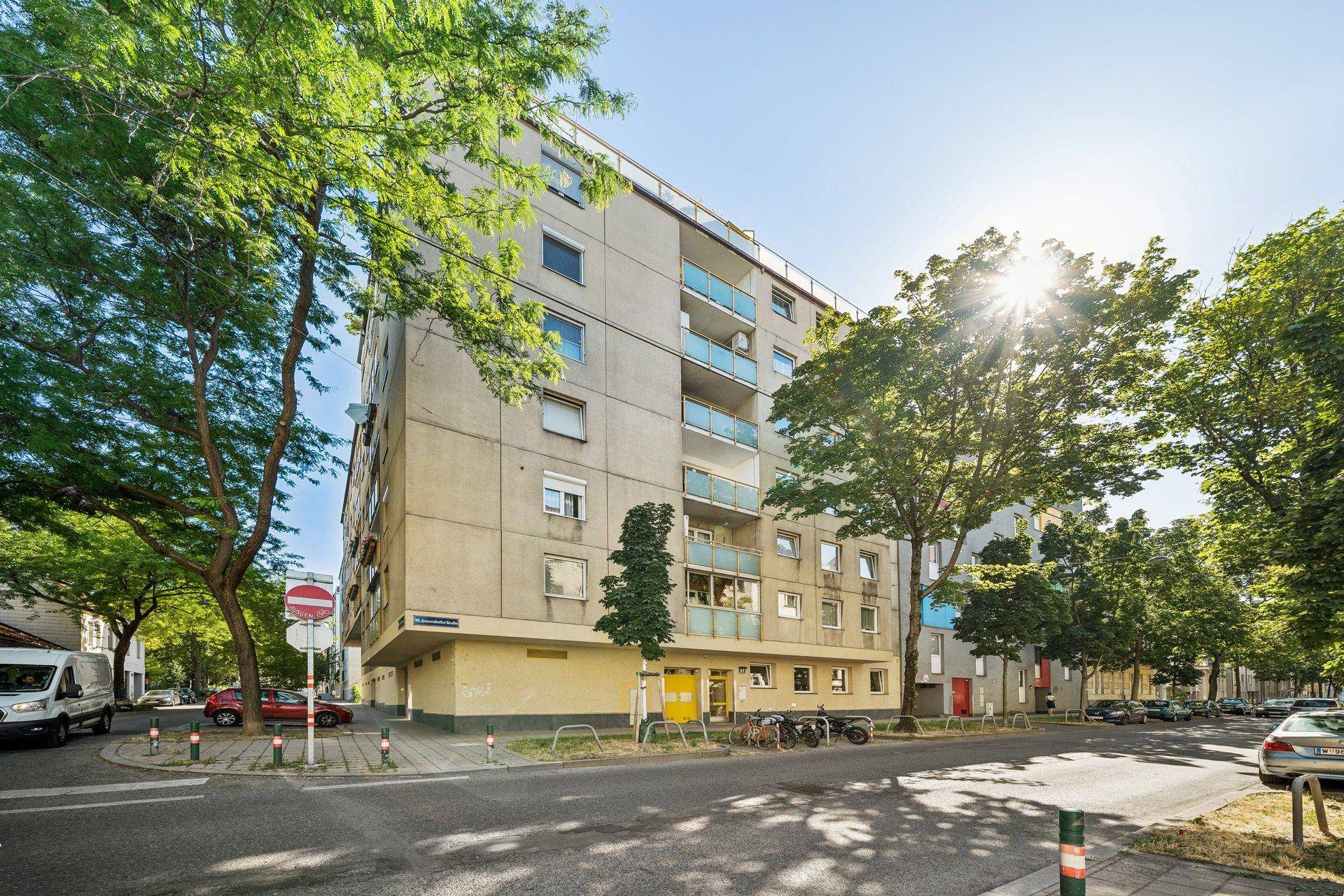 Mehrstöckiges Wohngebäude mit Balkonen und Bäumen an einer städtischen Straße.