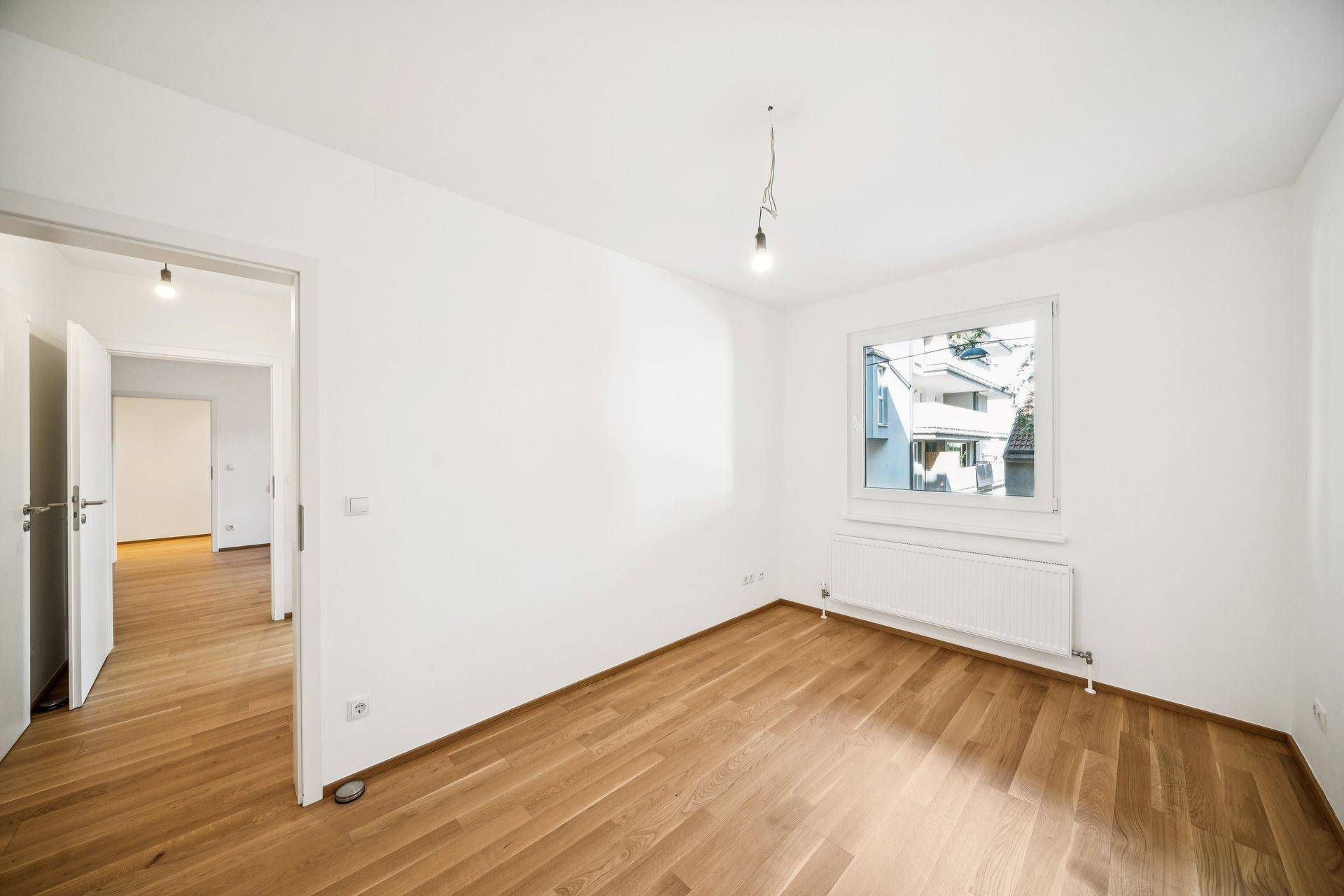 Heller Raum mit Parkettboden und einem Fenster, das viel Tageslicht hereinlässt.