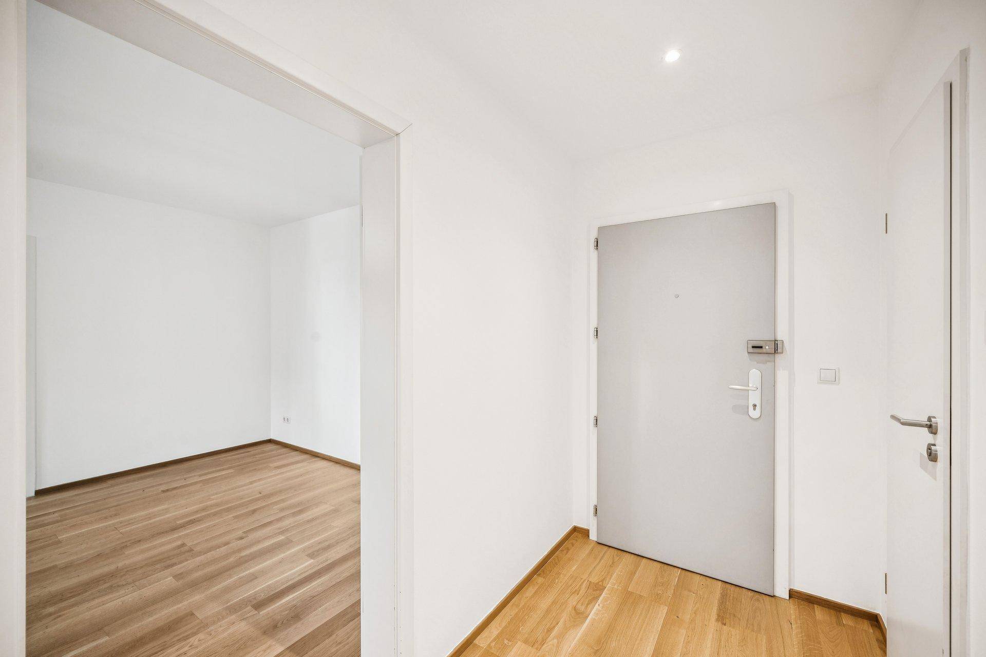 Heller Eingangsbereich mit Holzboden und einer modernen, schlichten Wohnungstür.