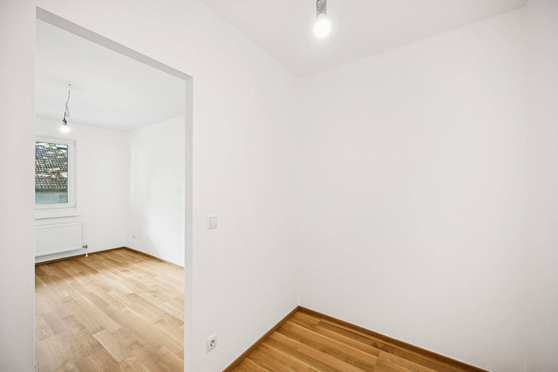 Heller Innenraum mit Holzboden und offenem Zugang zu einem weiteren Zimmer.