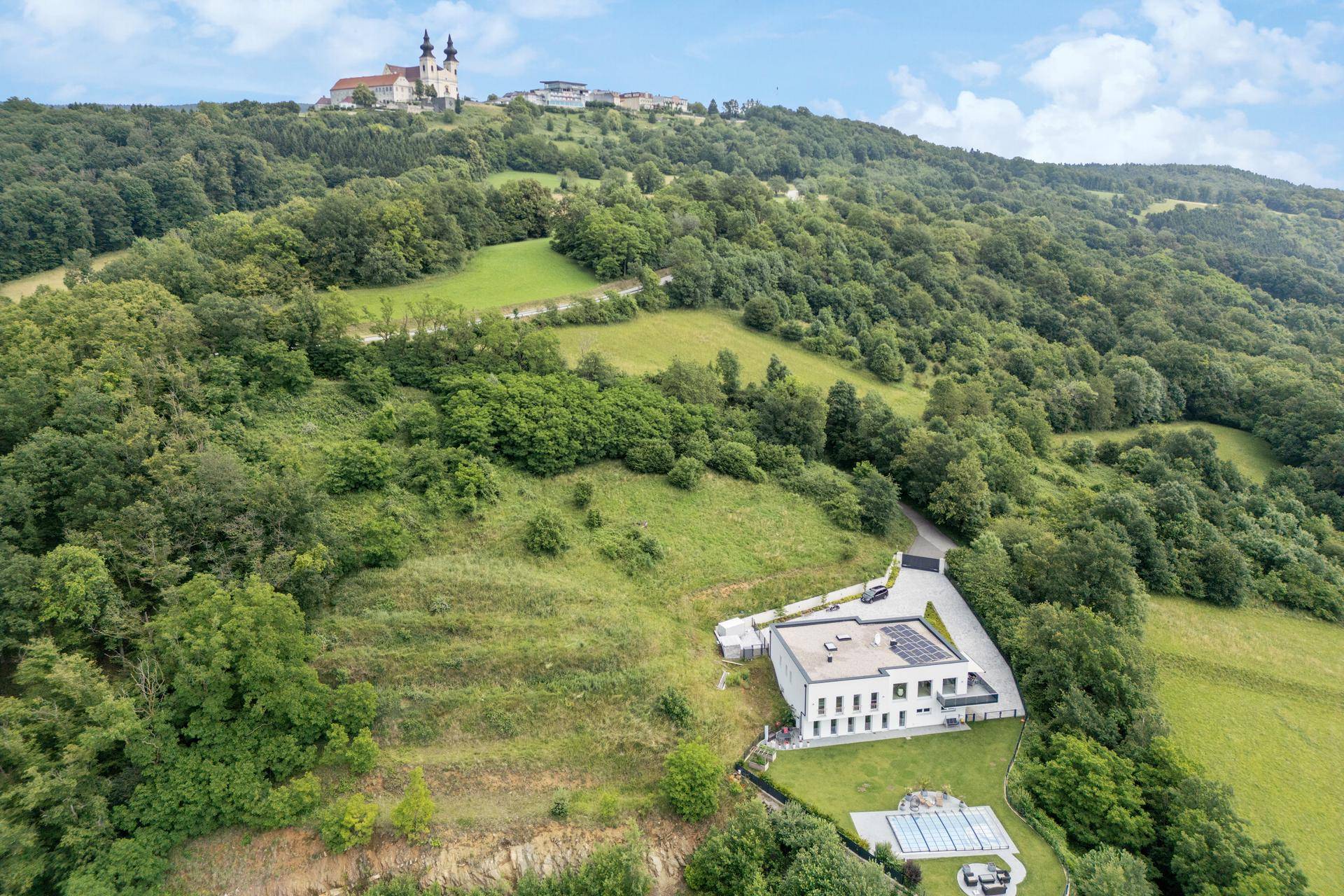 Luftaufnahme des Anwesens in idyllischer Hanglage mit Blick auf die umliegende grüne Landschaft und ein Kloster.