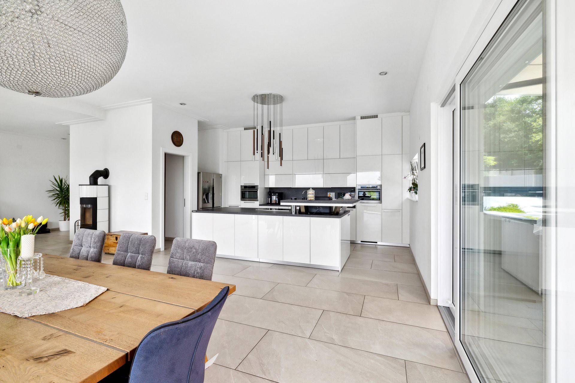 Moderne, offene Küche mit weißen Hochglanzfronten, Kücheninsel und Zugang zur Terrasse.