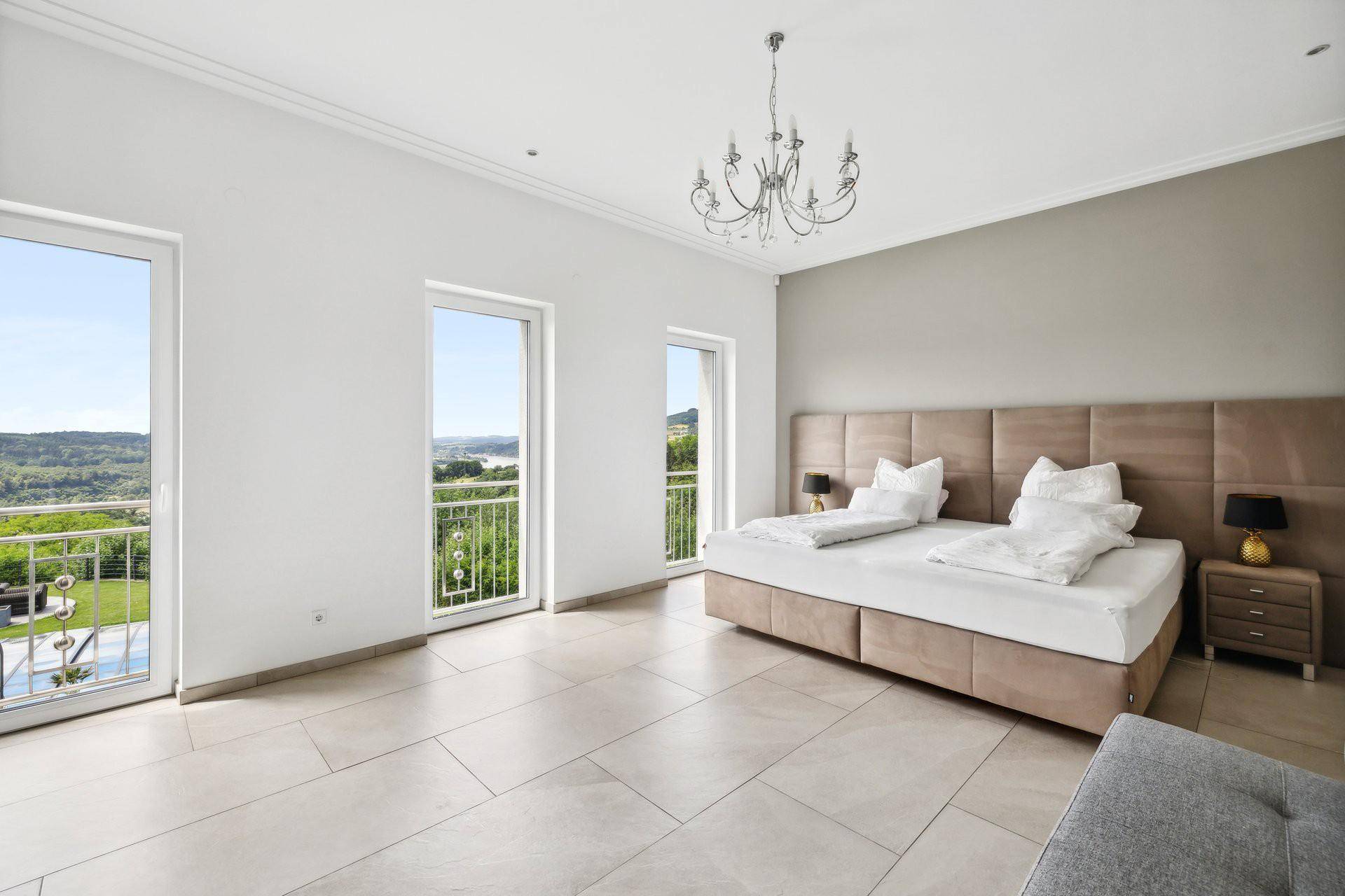Helles Schlafzimmer mit großen Fenstern, Fliesenboden und Zugang zu französischen Balkonen mit Weitblick.