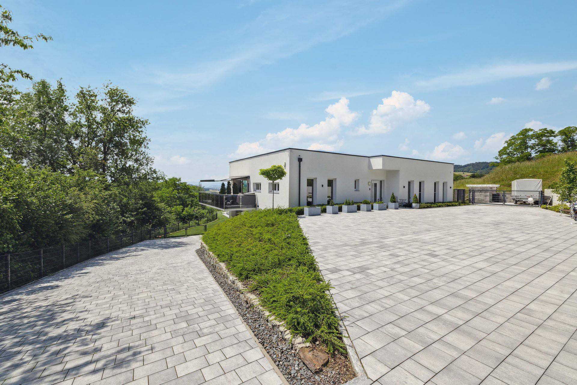 Moderne Hausfassade mit großzügiger gepflasterter Auffahrt und gepflegter Grünfläche.