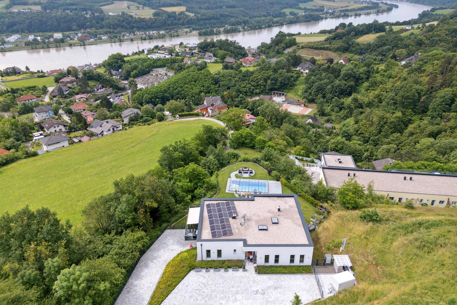 Weitläufige Luftaufnahme des modernen Anwesens mit Pool und Photovoltaikanlage, eingebettet in grüne Hügel.