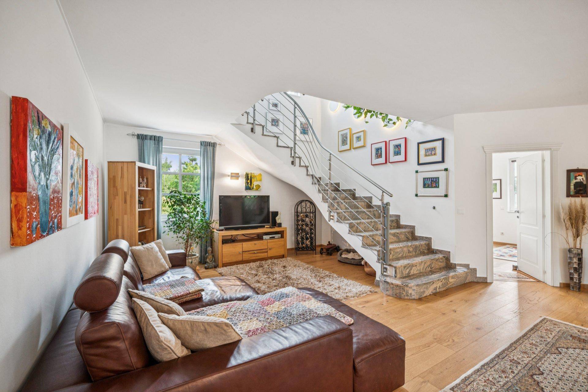 Gemütliches Wohnzimmer mit Ledersofa, Holzfußboden und eleganter Wendeltreppe aus Stein.