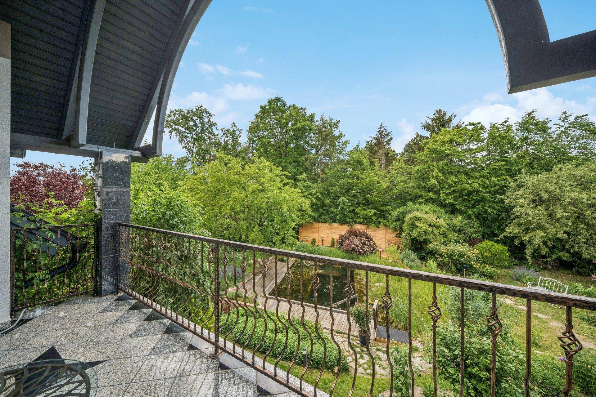 Balkon mit schmiedeeisernem Geländer und weitem Blick über den Garten und die umliegende Natur.