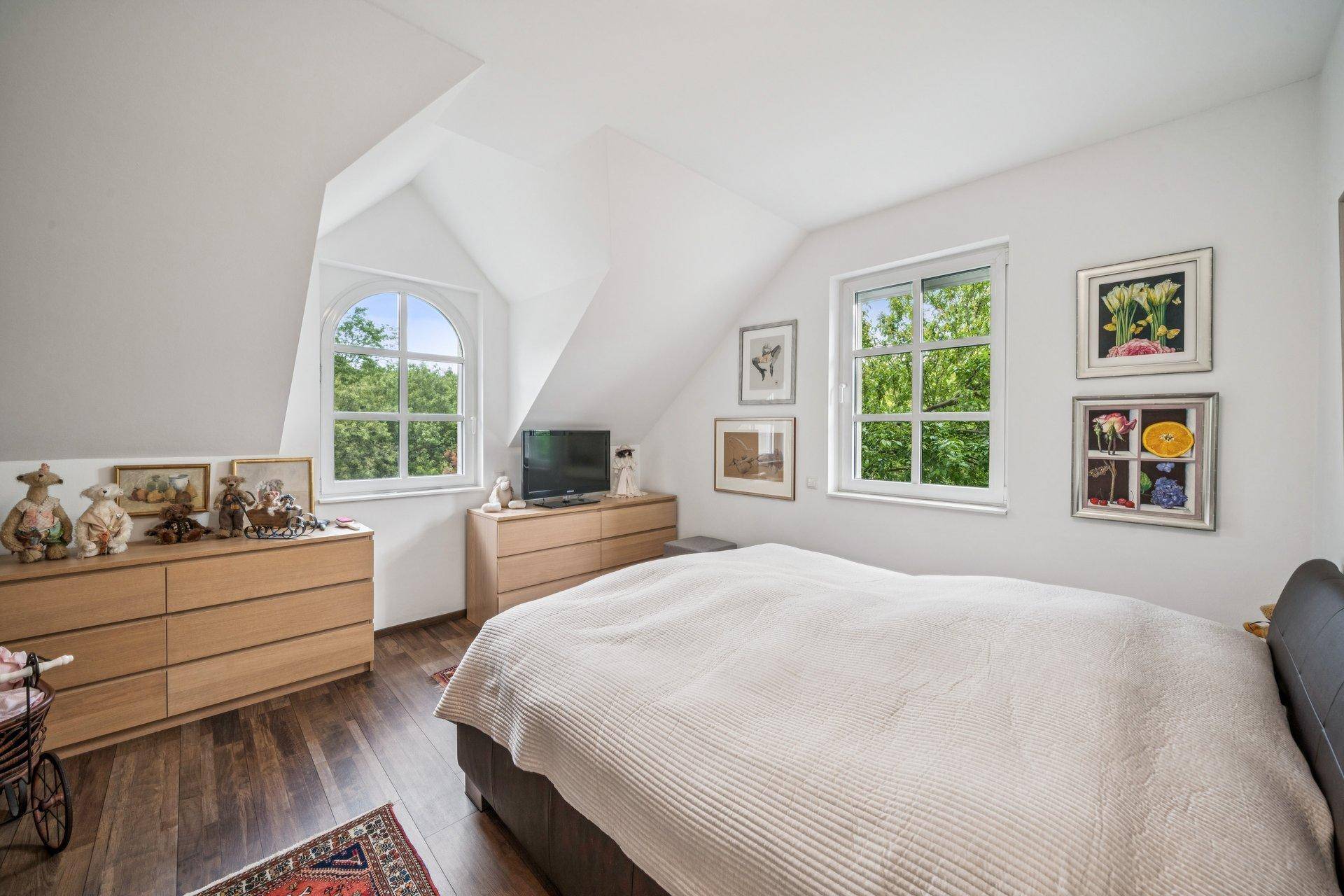 Helles Schlafzimmer im Dachgeschoss mit Holzboden, Kommoden und Fenstern mit Blick ins Grüne.