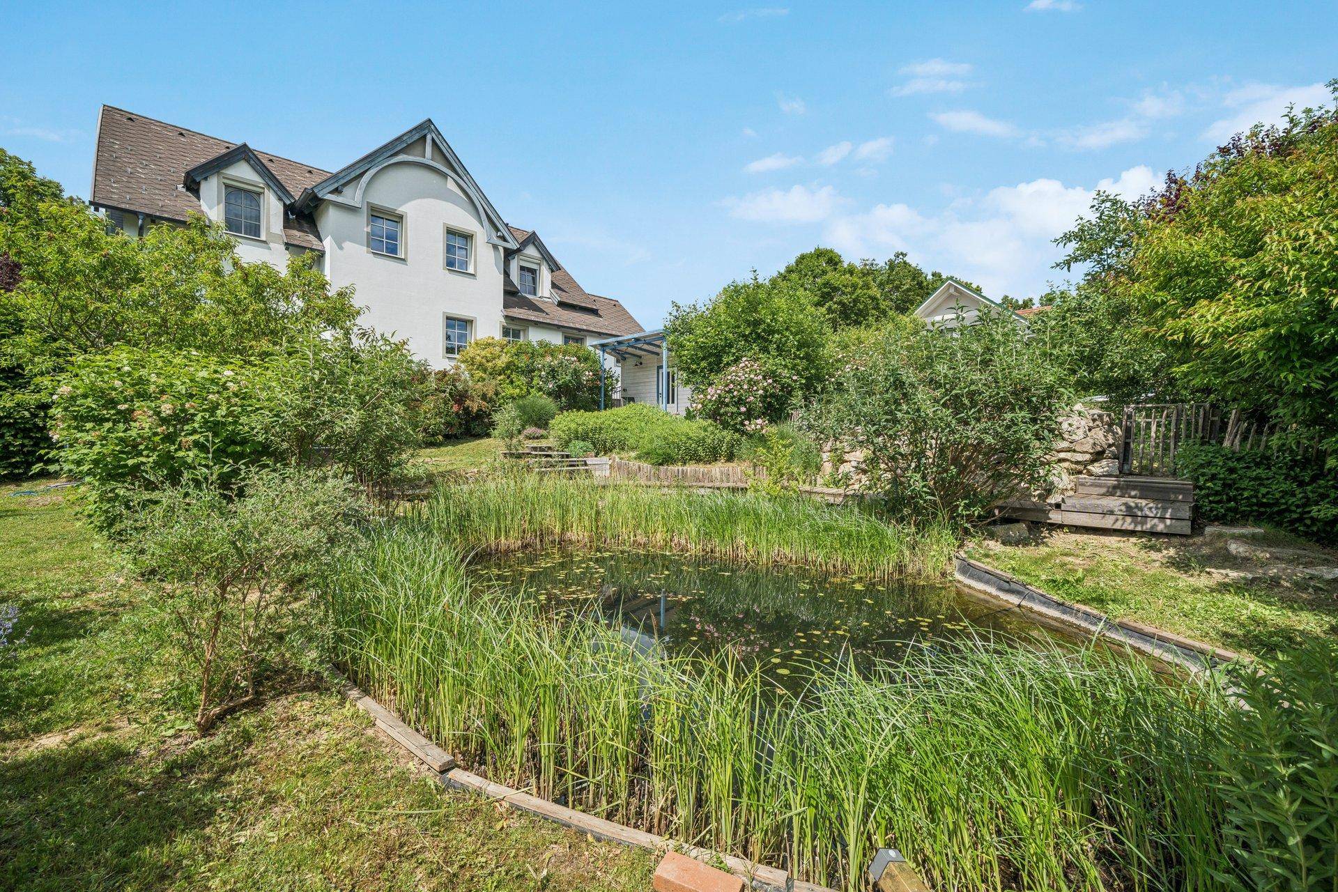 Malerischer Gartenbereich mit Teich und vielfältiger Bepflanzung, umgeben von grüner Natur.