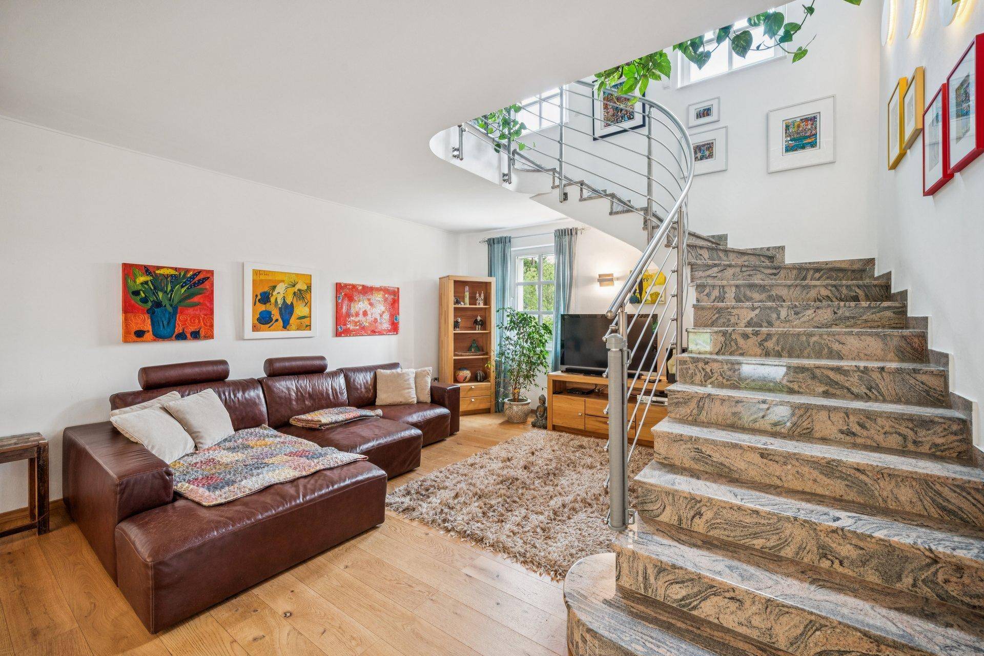 Gemütliches Wohnzimmer mit Ledersofa, Holzfußboden und eleganter Wendeltreppe aus Stein.