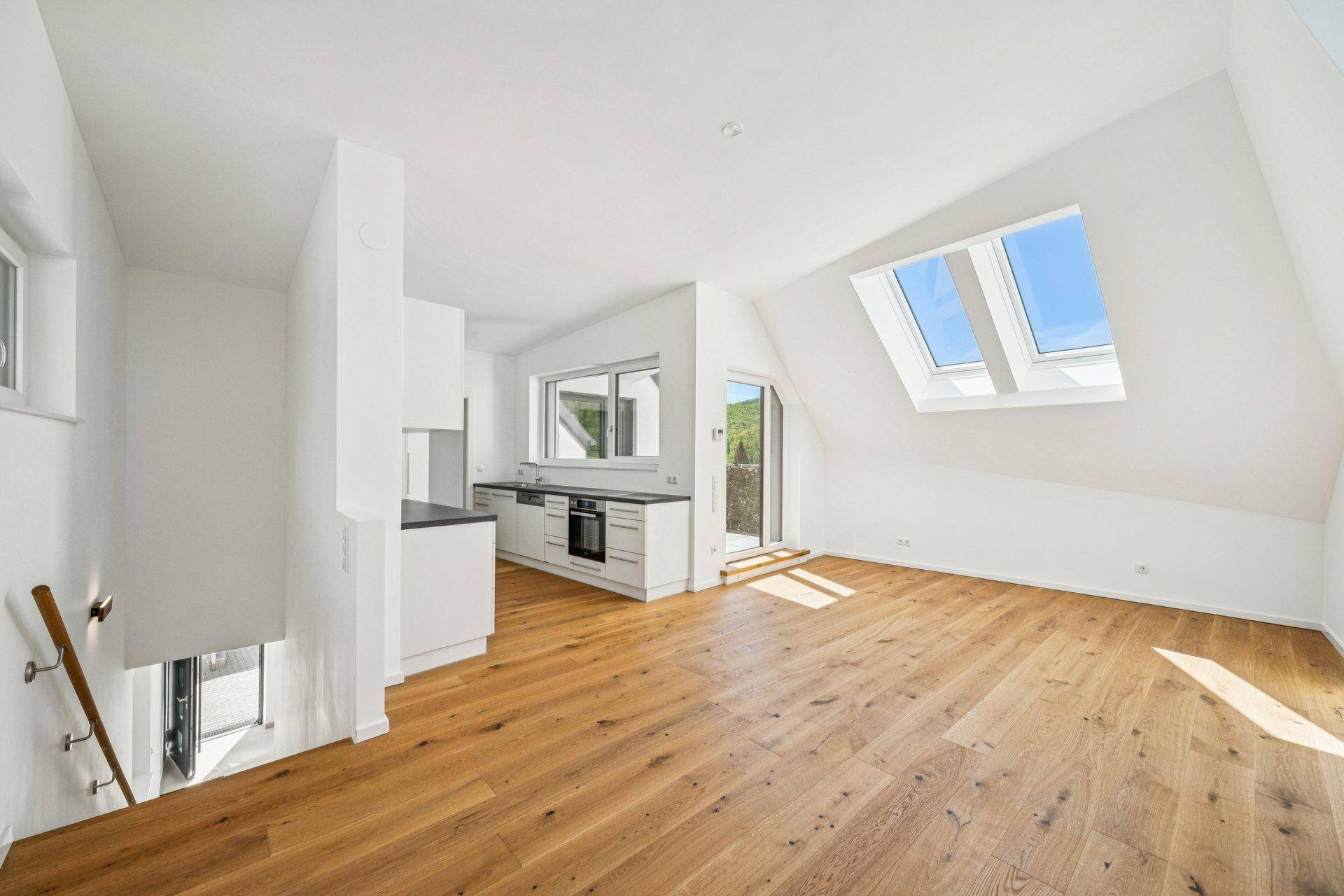 Heller offener Wohnbereich mit integrierter Küche, Holzboden und Dachfenstern für viel Tageslicht.