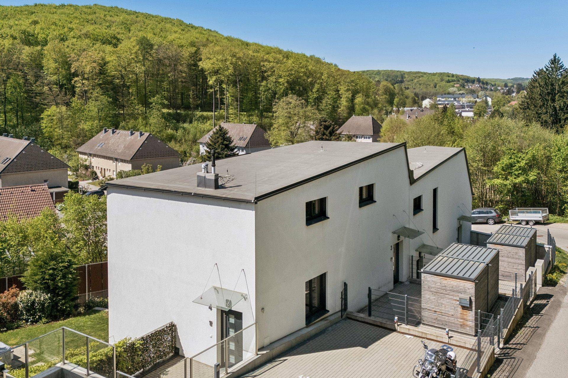 Luftaufnahme eines modernen Gebäudes mit Flachdach, umgeben von viel Grün und anderen Wohnhäusern.